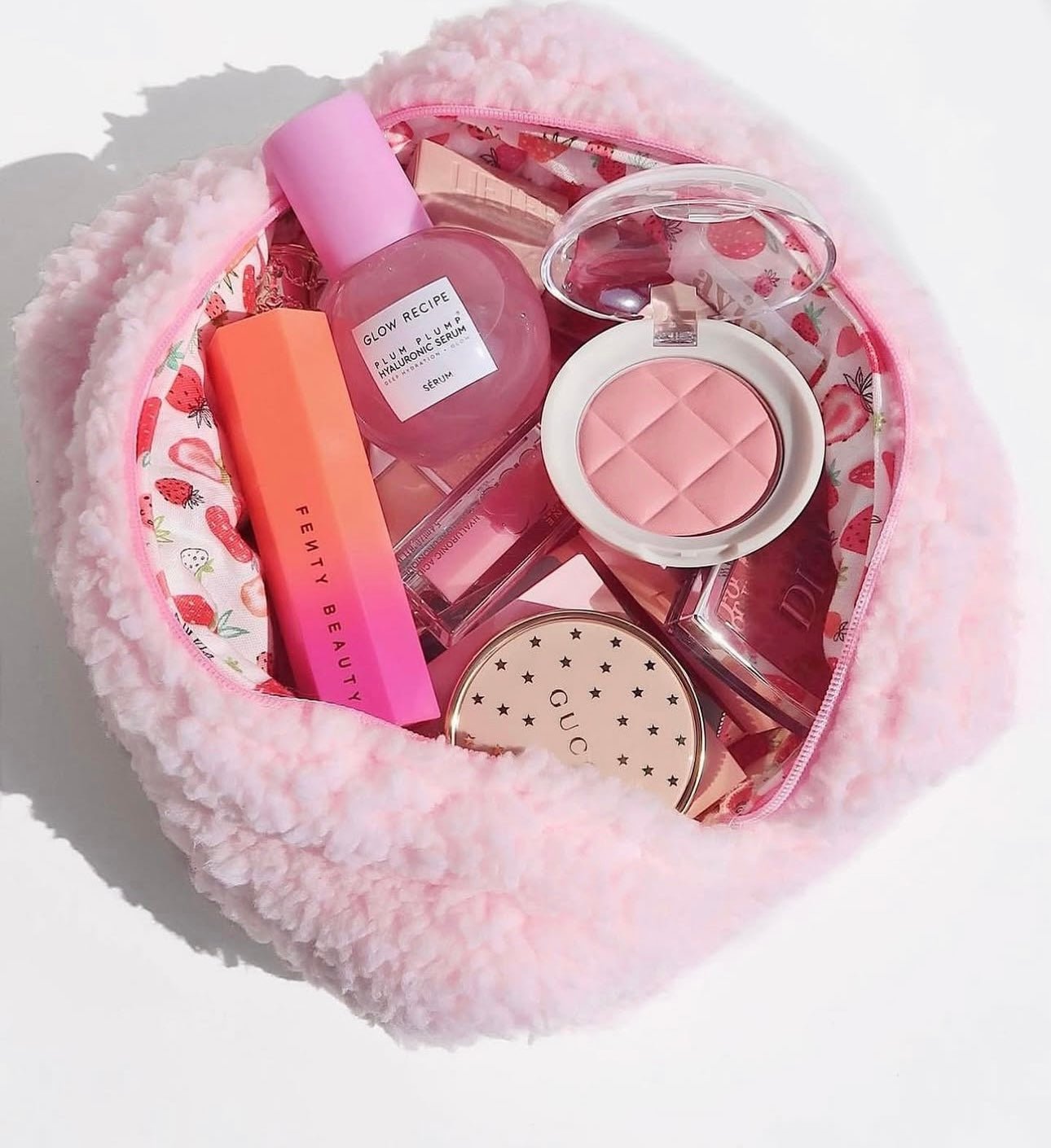 Pink fluffy pouch with strawberry-lined zip opening, holding cosmetics.