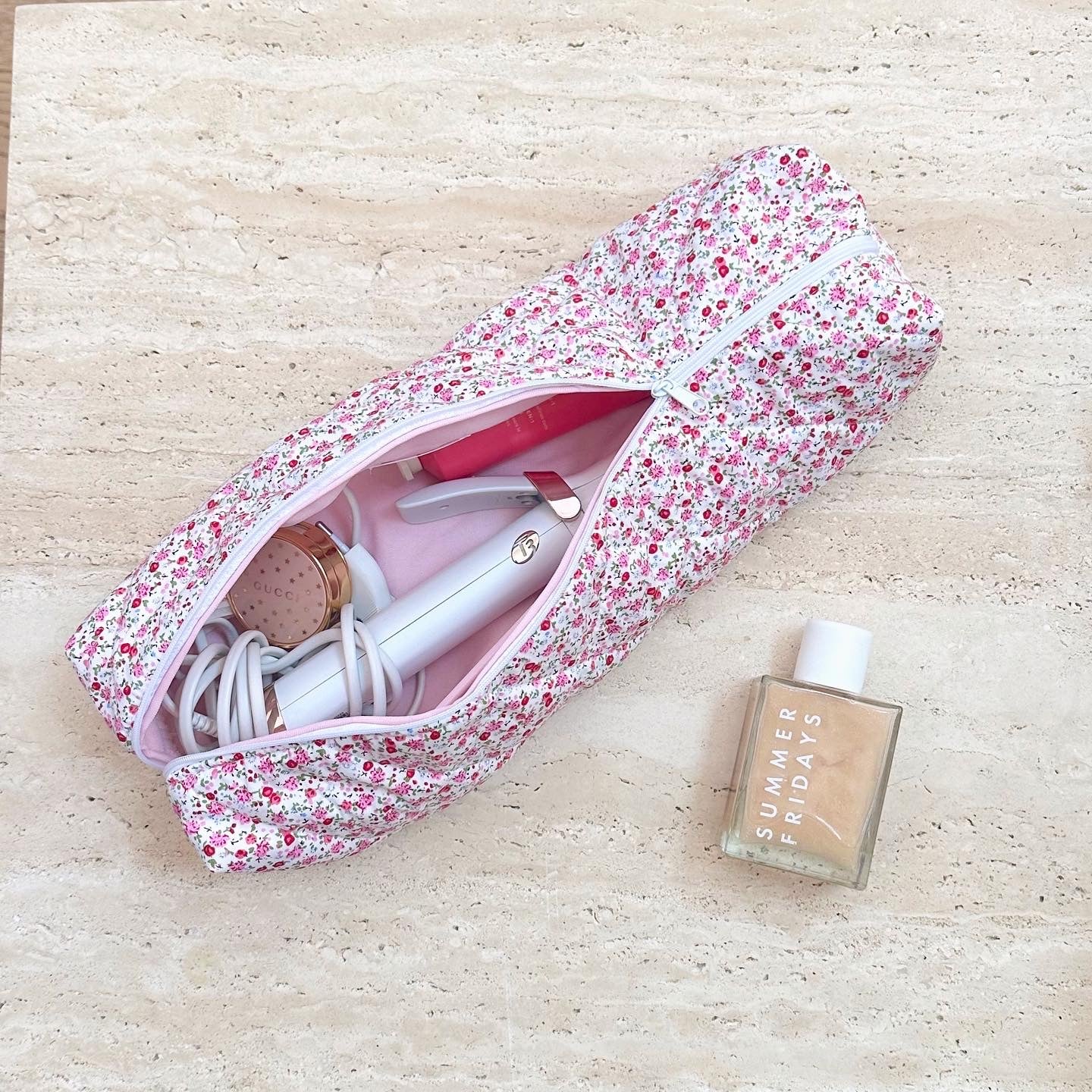 Floral toiletry bag with open zipper, pink interior and assorted toiletries visible inside.