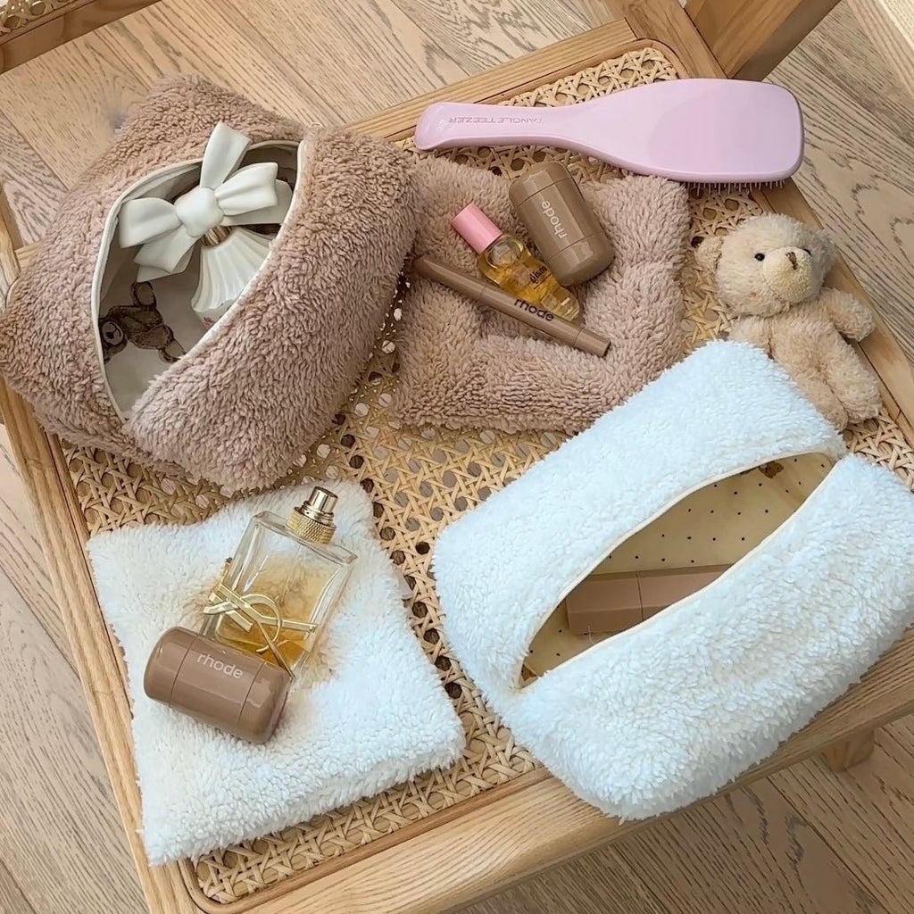 Camel teddy and white teddy zip pouches in a woven tray with grooming bottles.