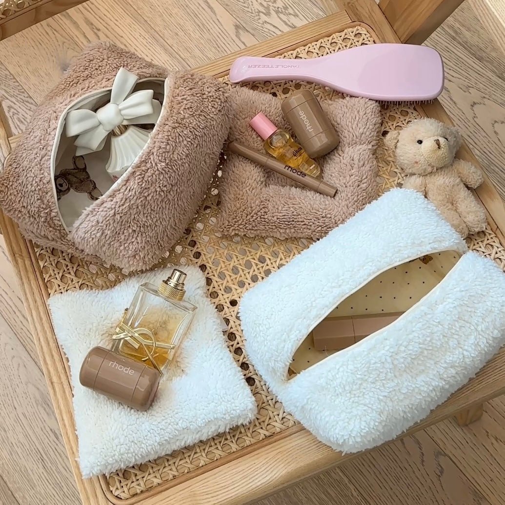 Camel teddy and white teddy zip pouches in a woven tray with grooming bottles.