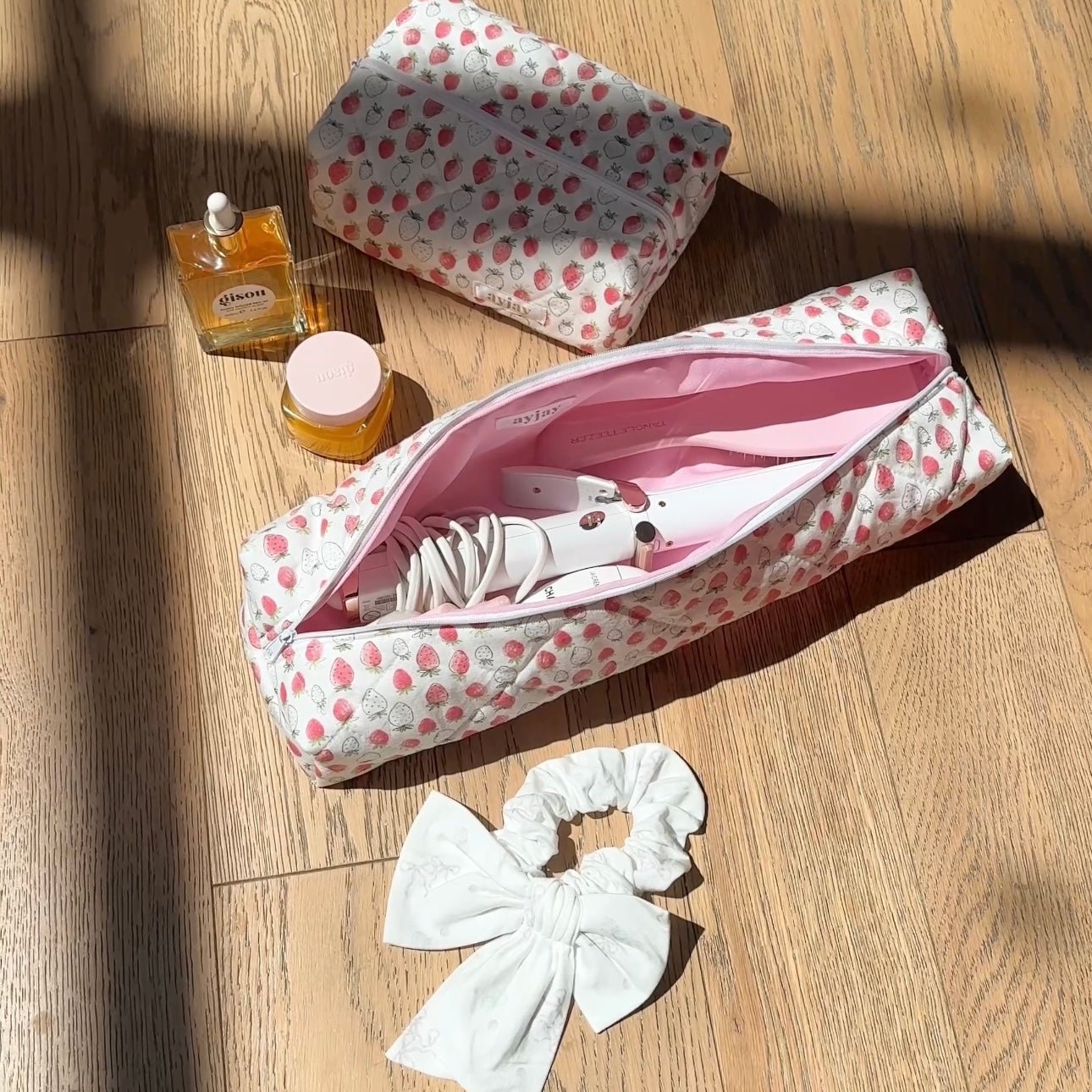 Strawberry-print pouch open with white hair tool and bow scrunchie