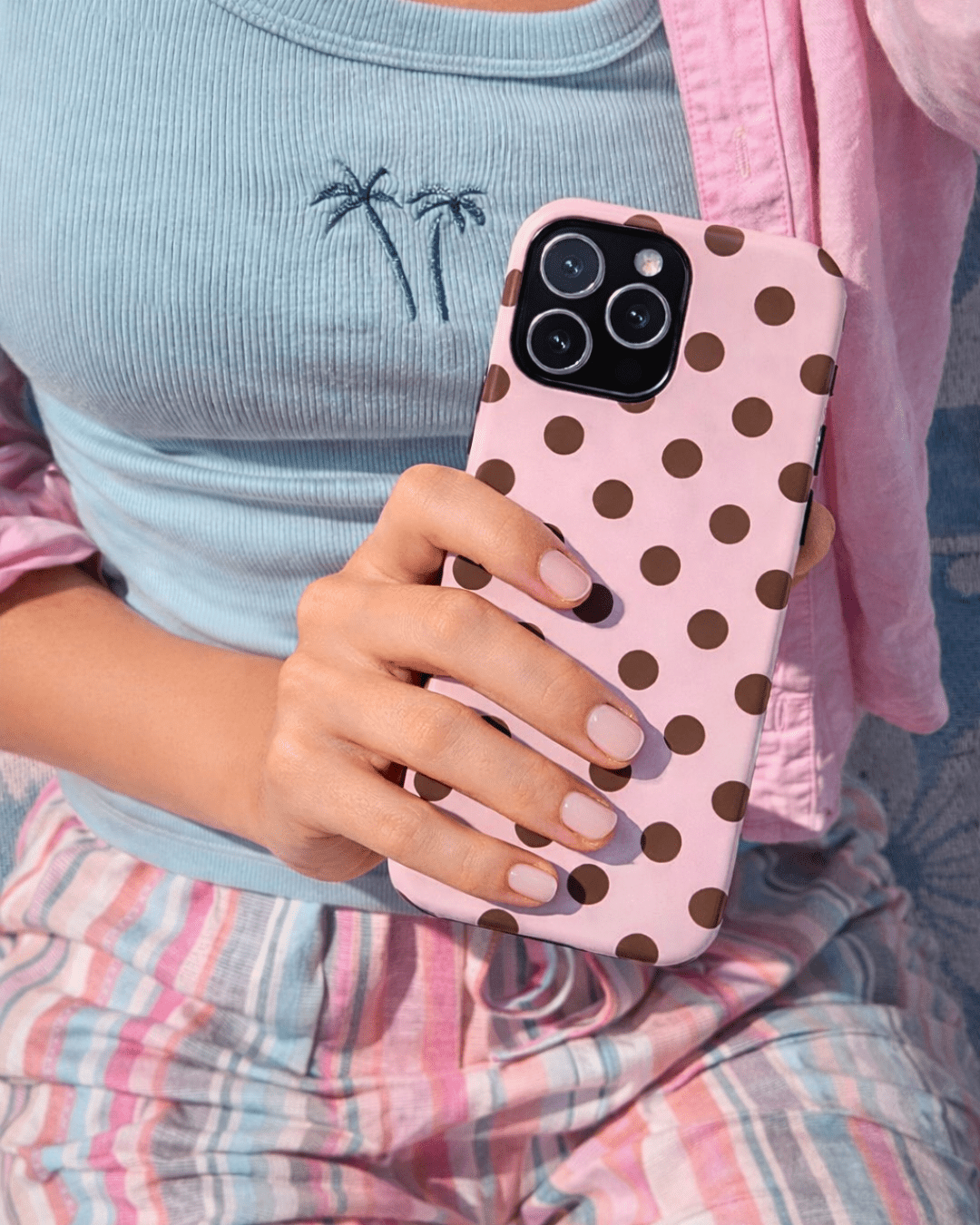 Pink polka dot phone case held in hand with four camera cutouts