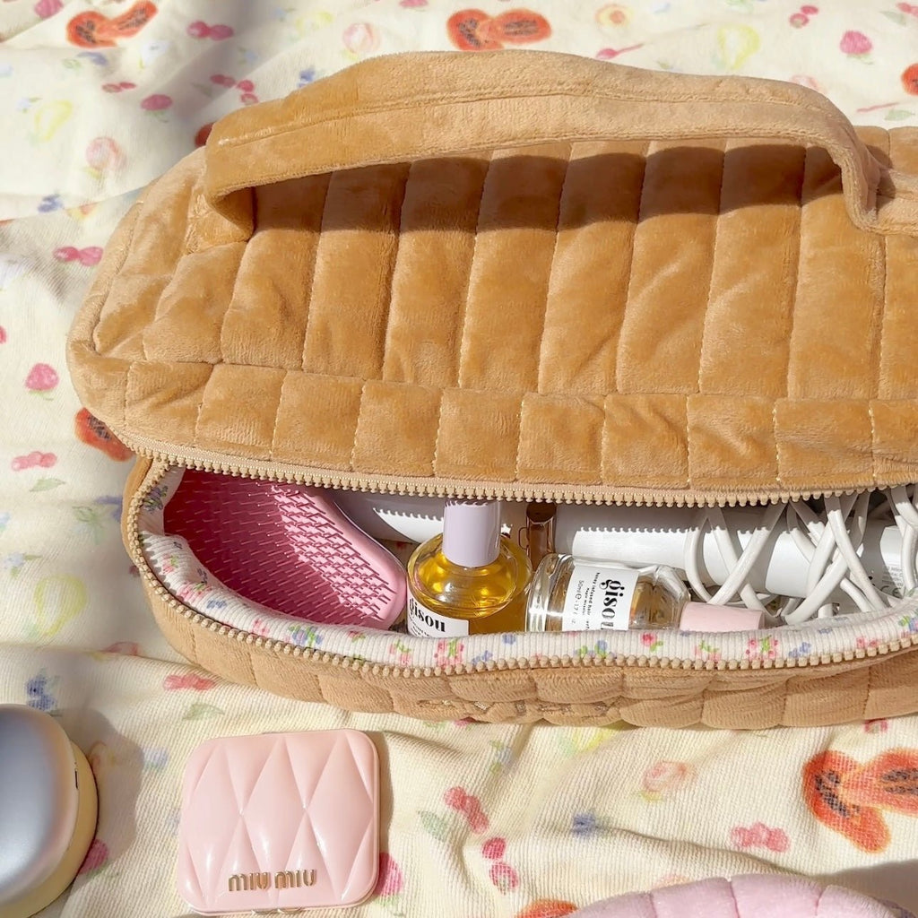 Top view of tan quilted vanity bag, open to compartments with bottles and cords.