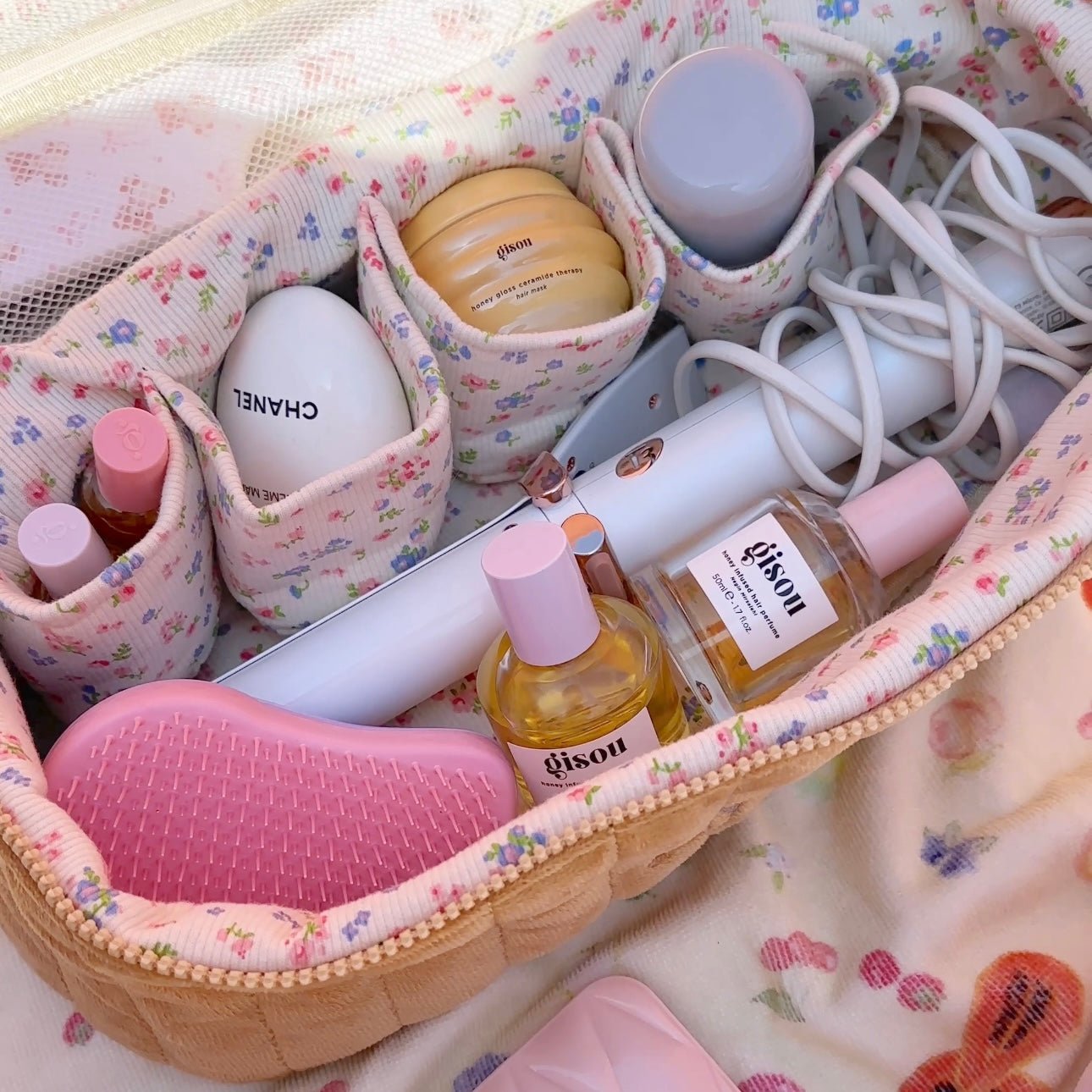 Open tan floral vanity hair tool bag with bottles, brushes, and cord organizers.