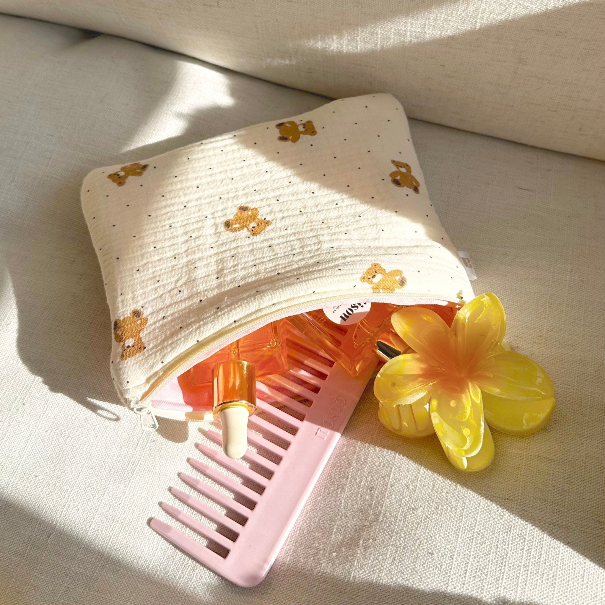 Cream teddy bear dotted pouch, open to reveal pink comb and small bottles