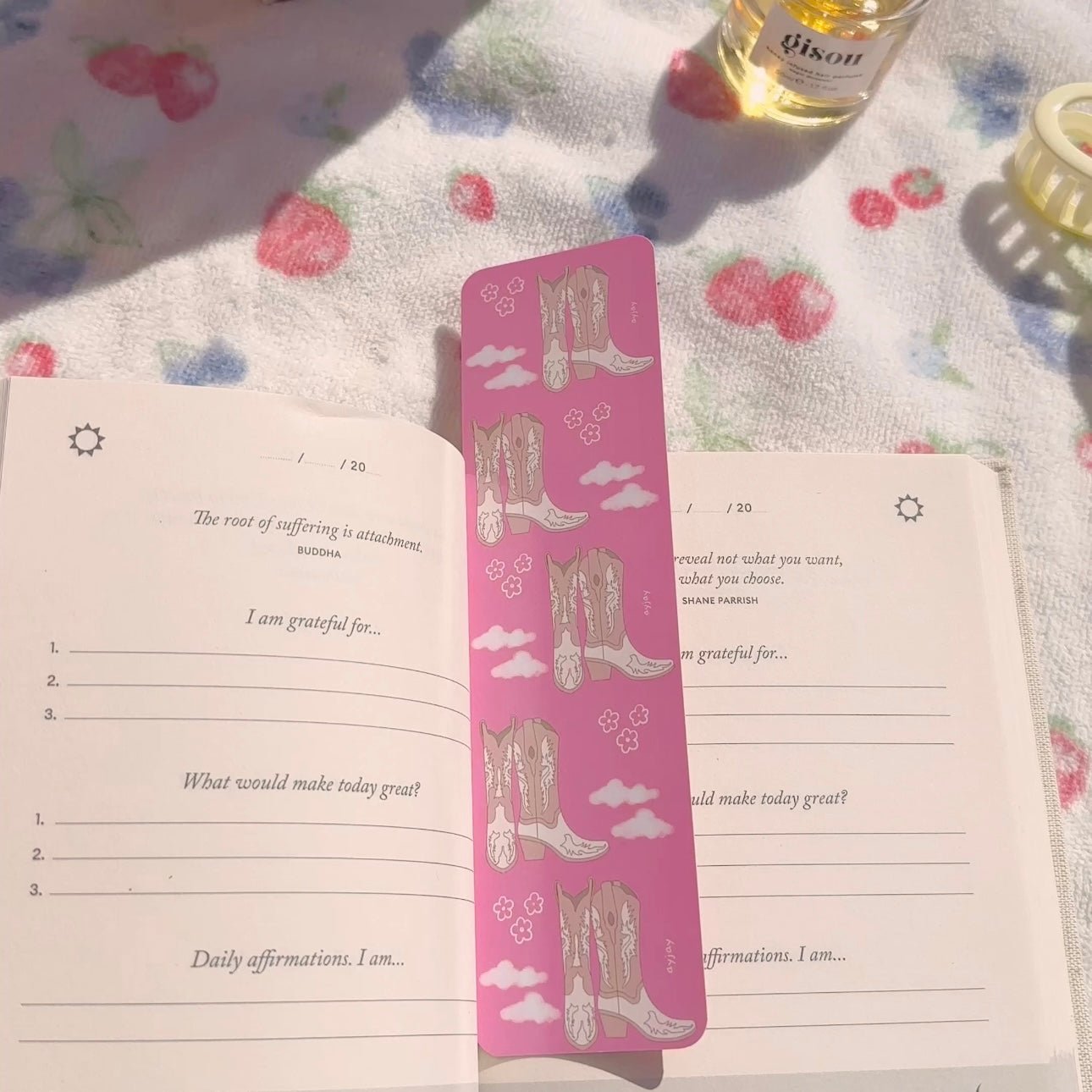 Pink paper bookmark with cowgirl boots and clouds, placed between journal pages.