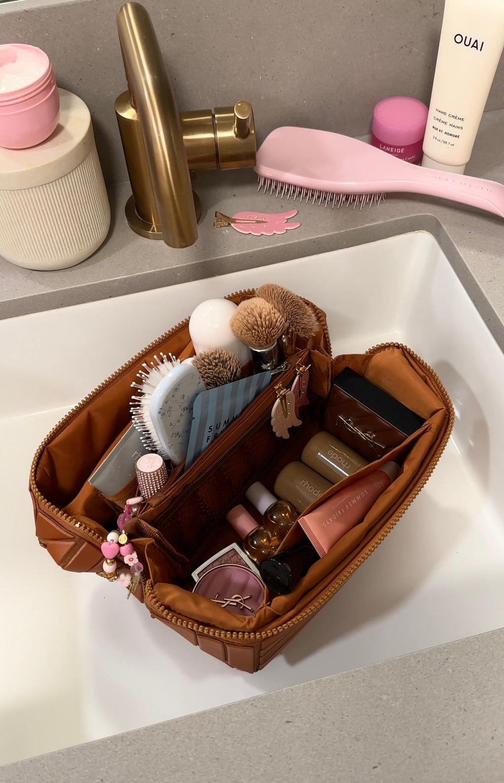 Mocha-brown XL makeup case open in sink area, with brushes, lip products, and bottles
