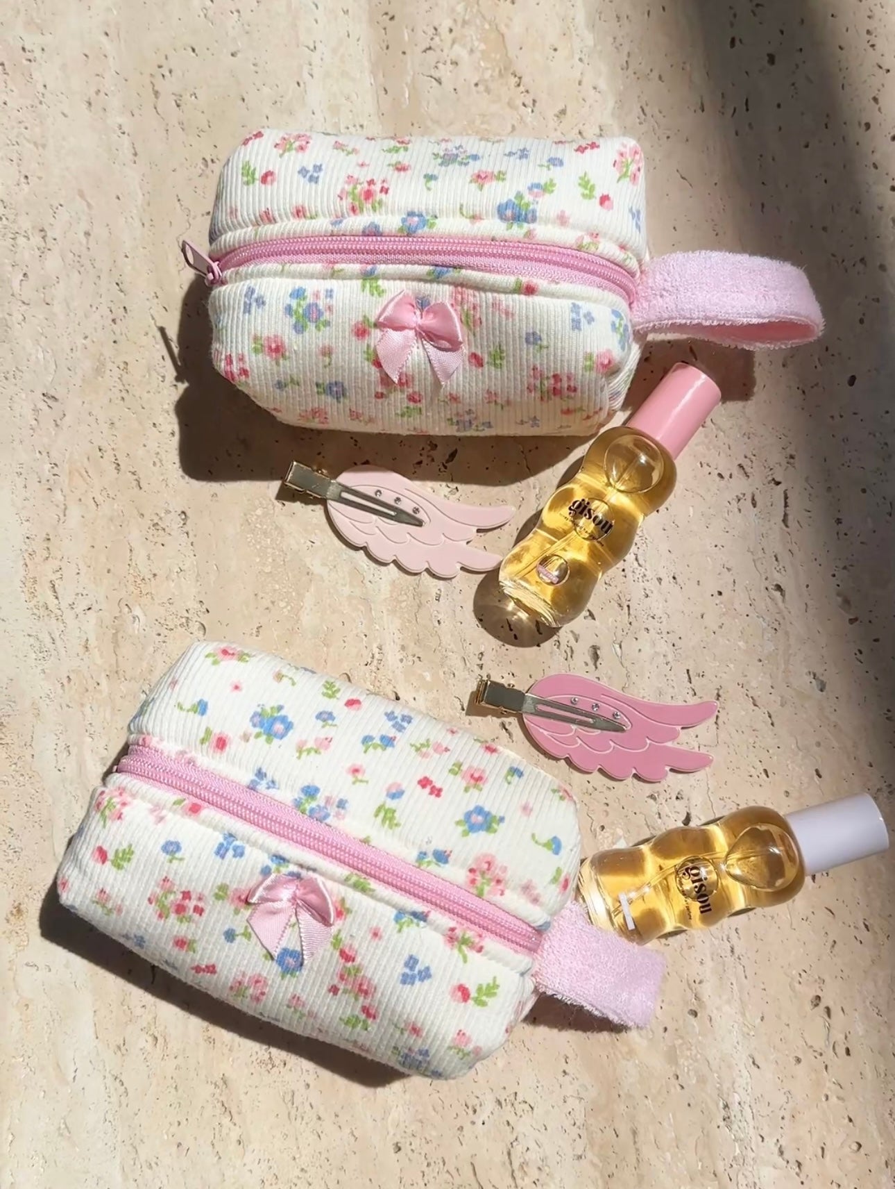 Two cream floral pouches with pink zipper and bow charm, laid on light surface