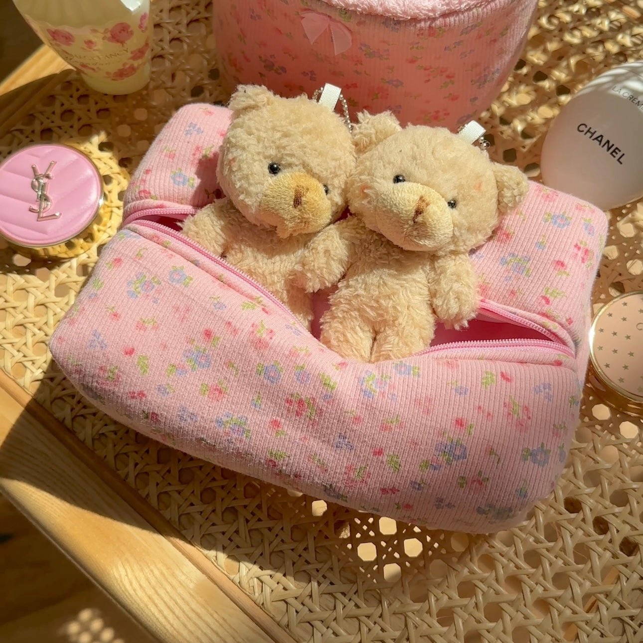 Pink floral-patterned tube pillow with two beige teddy bears tucked inside