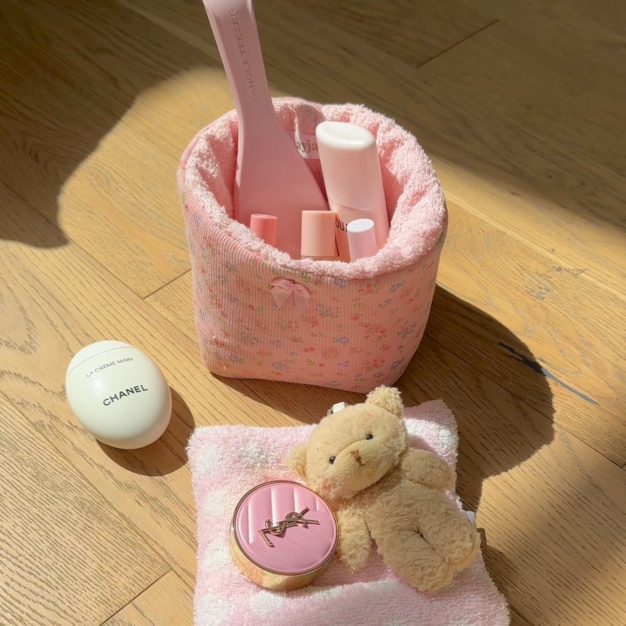 Pink floral fabric organizer basket with terry trim, open center, sitting on light wood floor