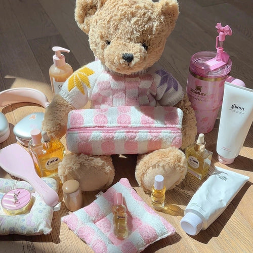 Small plush teddy bear in pink-and-white check outfit with soft folded towel