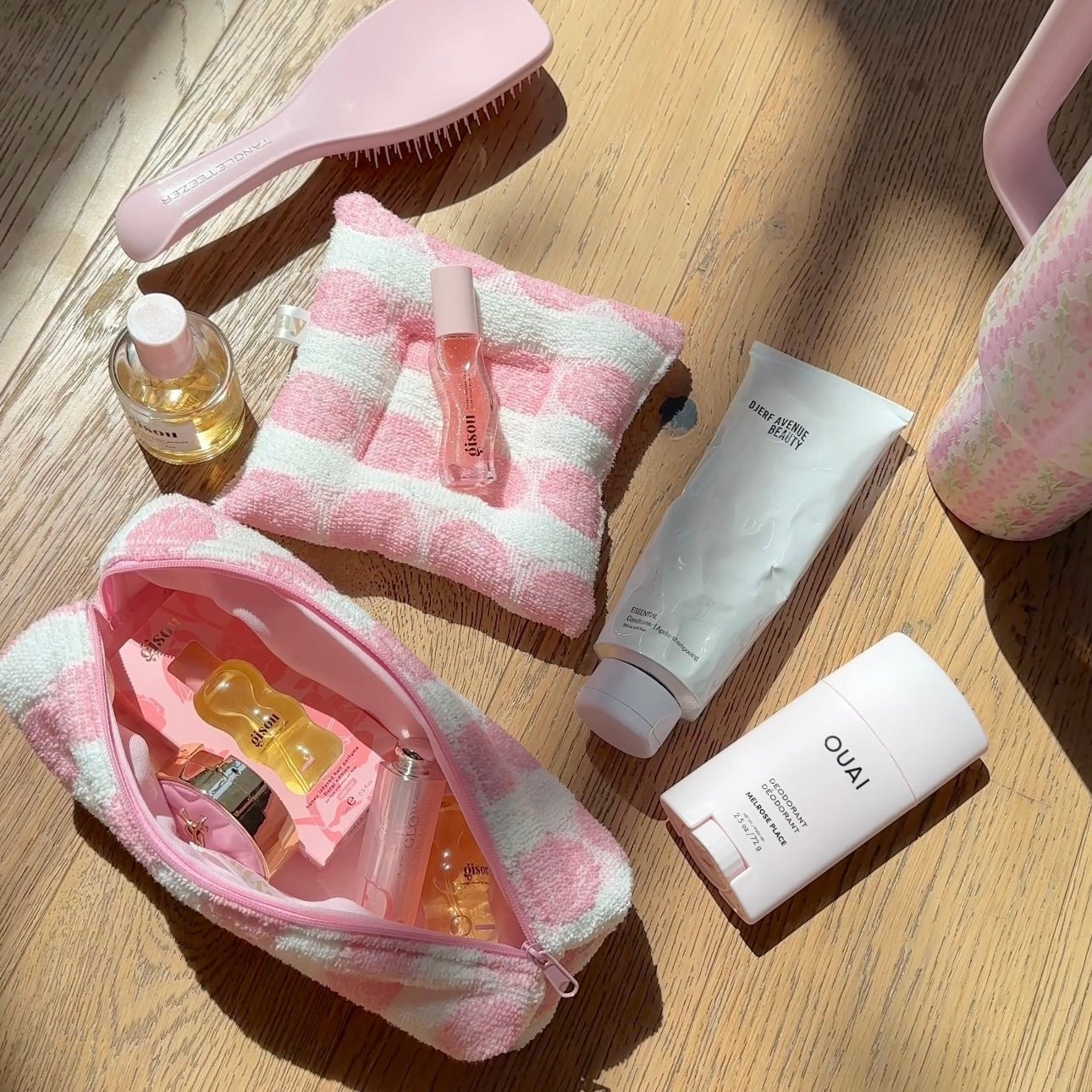Open pink-and-white check zip pouch with matching towel; bottles and tubes nearby