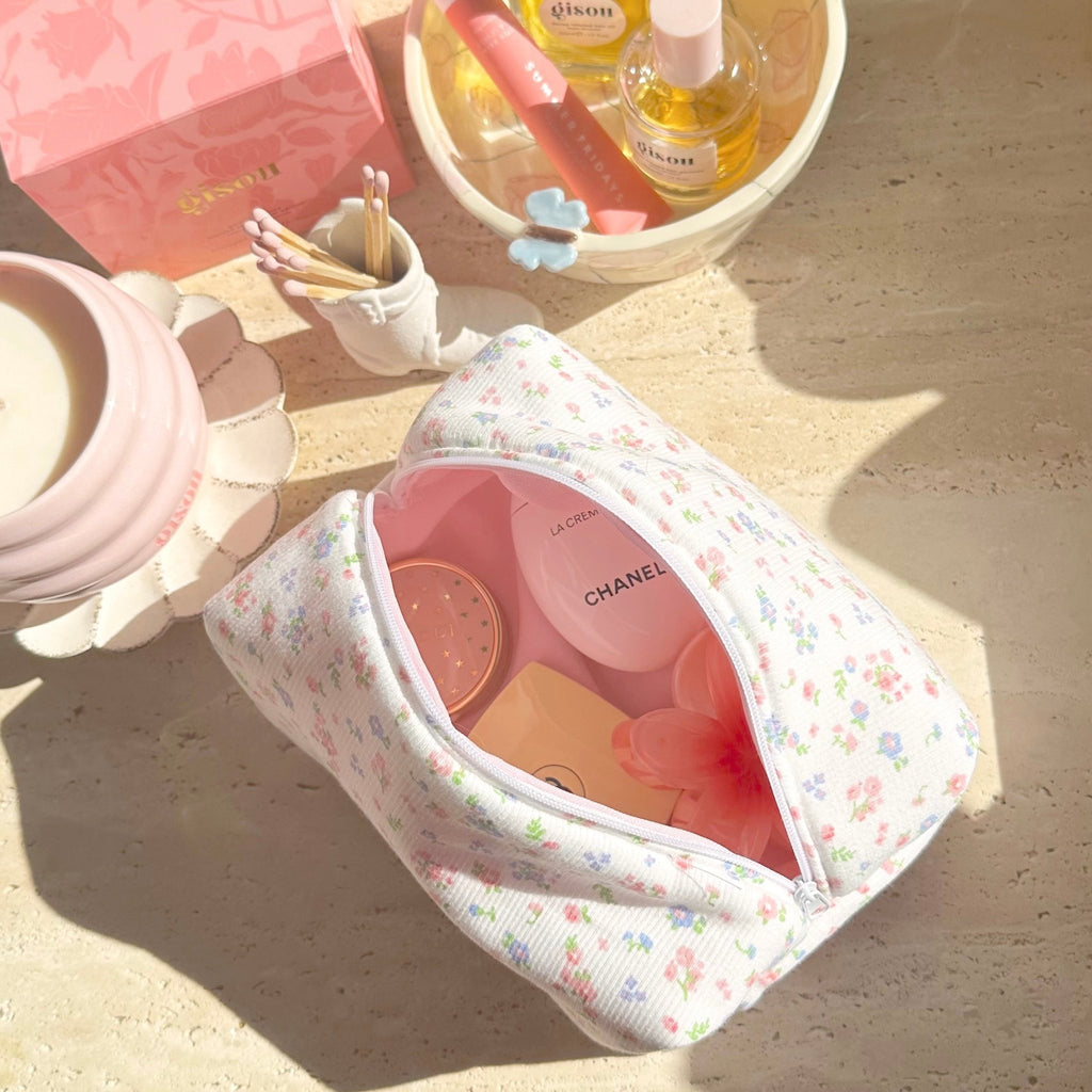 White floral zip pouch opened flat, pink lining and items in compartments