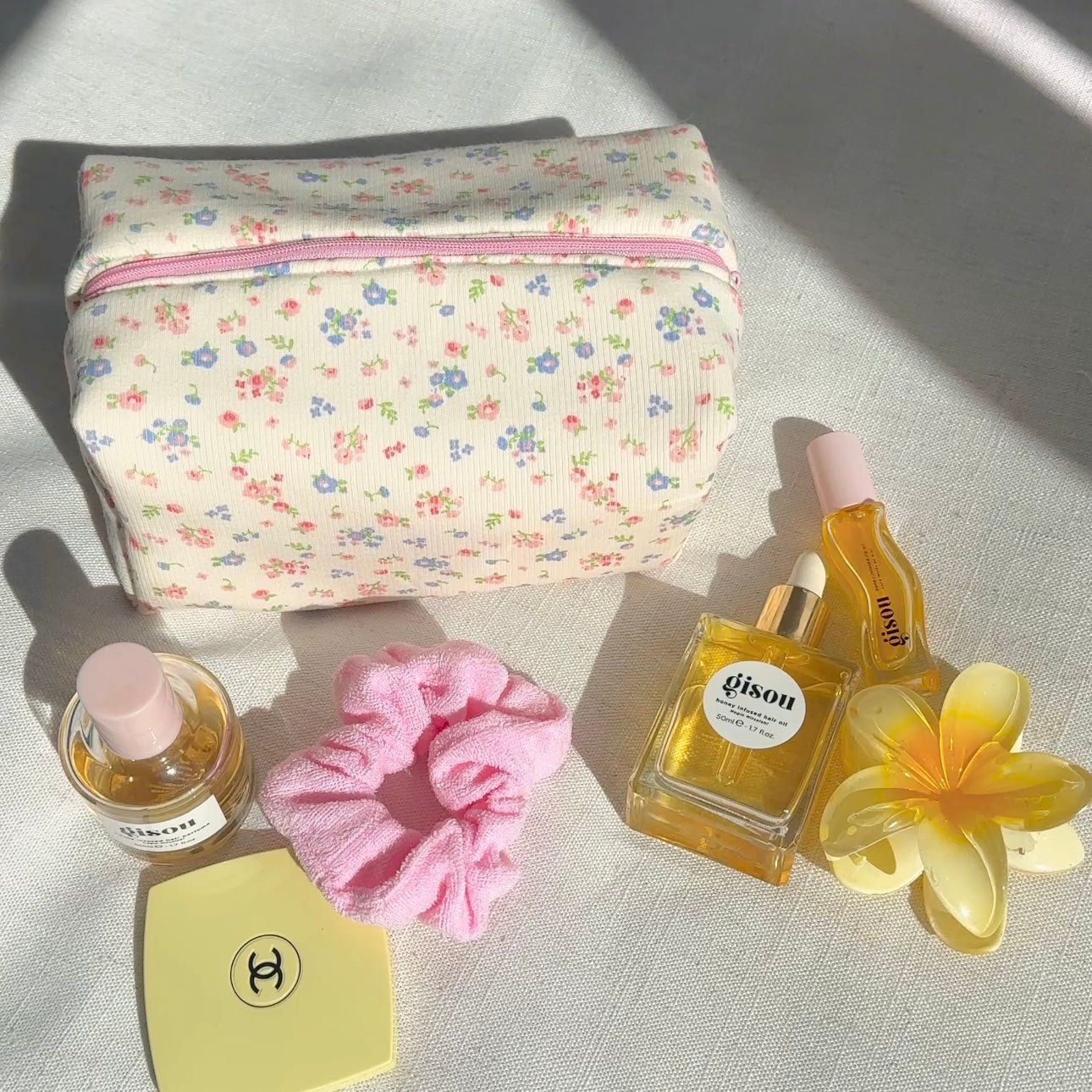 Small cream floral zip pouch with pink trim, with perfume bottles and scrunchie