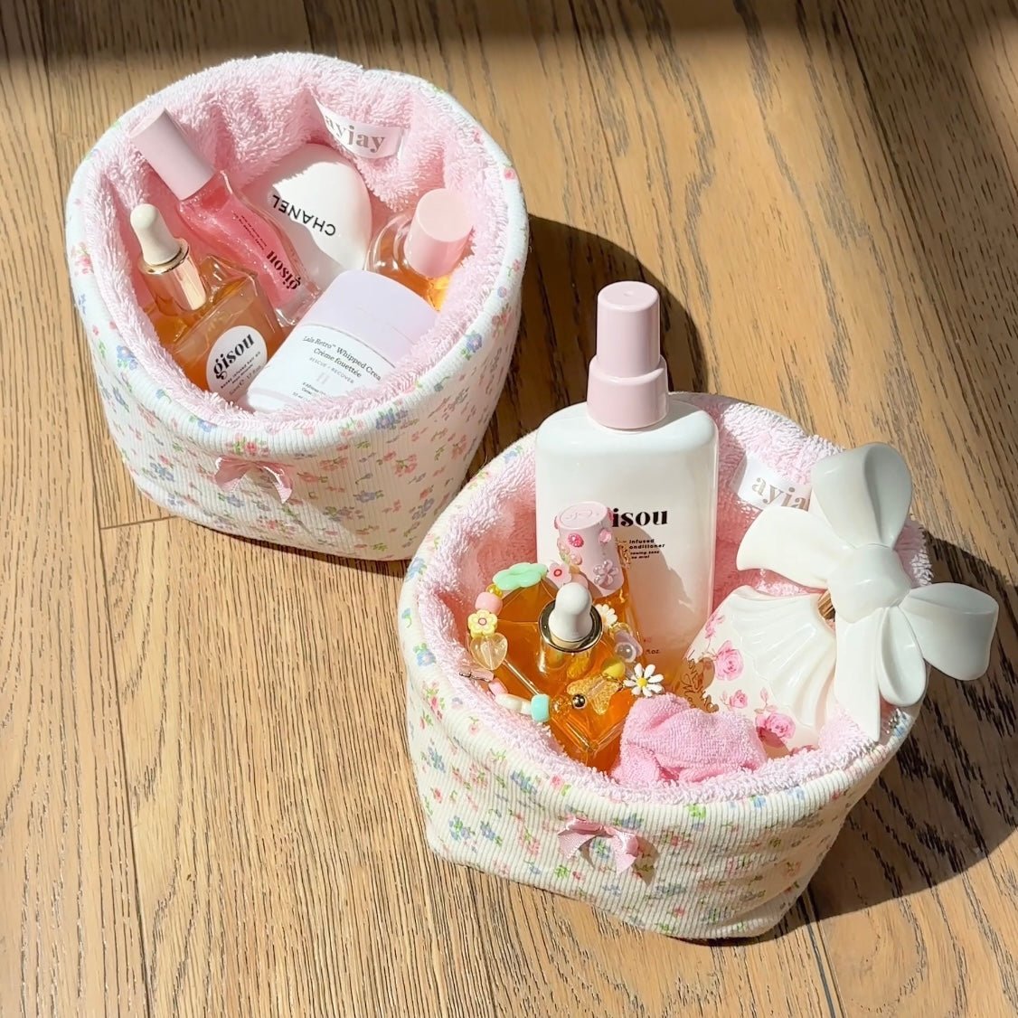 Two floral organizer baskets with pink interiors and bows on a wood floor