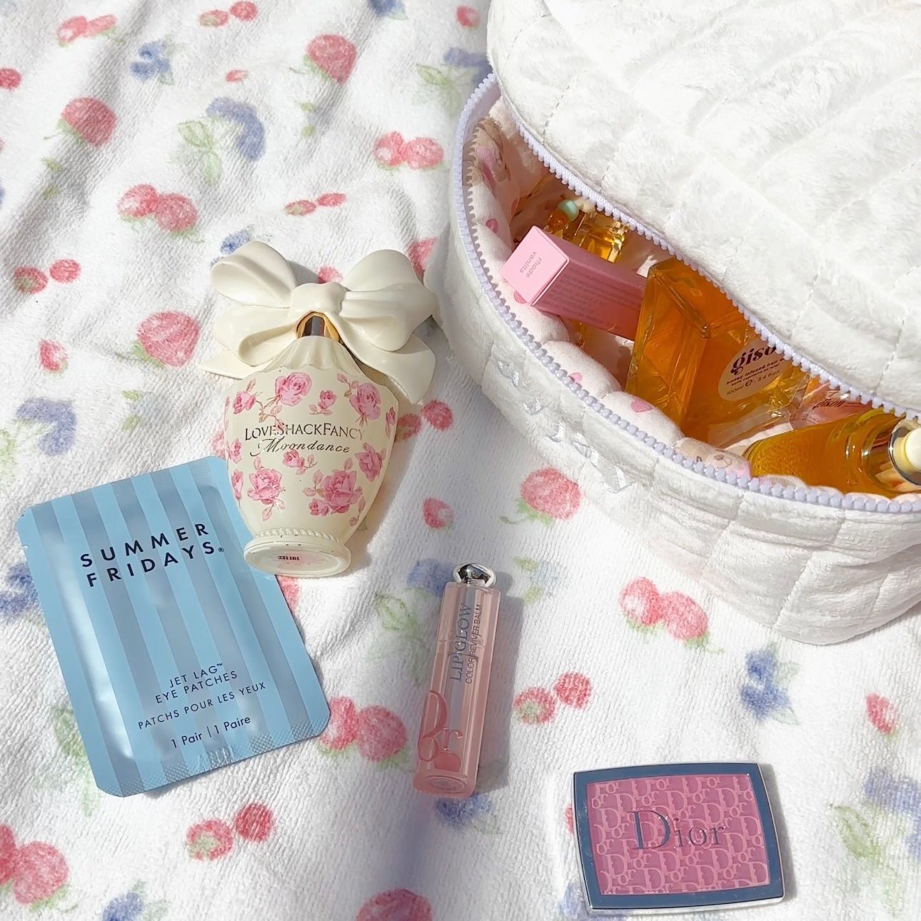 Close-up of open white plush vanity bag with pink heart lining and perfume bottles inside.