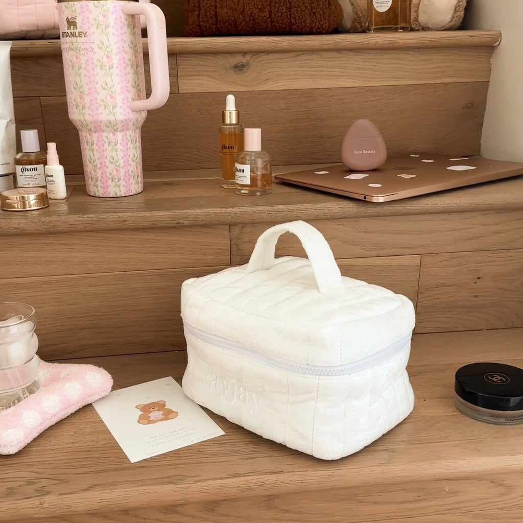 White plush vanity bag with handle, soft padded exterior and subtle stitched quilting.