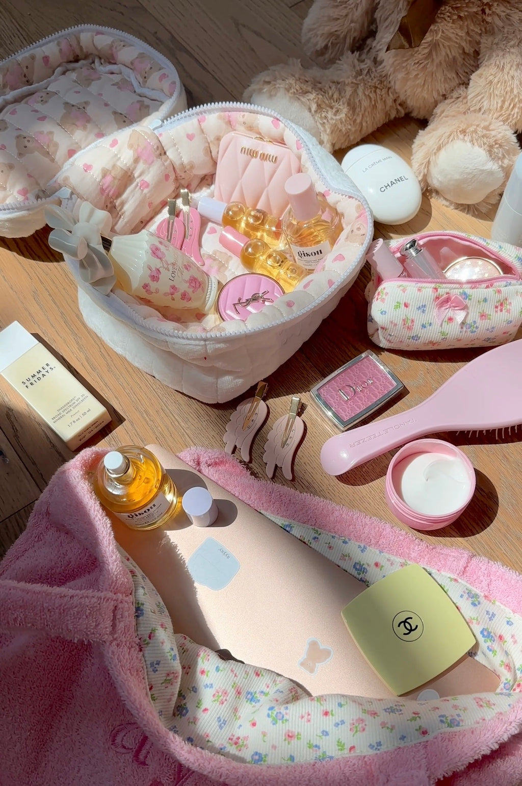 Open white plush vanity bag with pink heart print lining and multiple small beauty bottles inside.