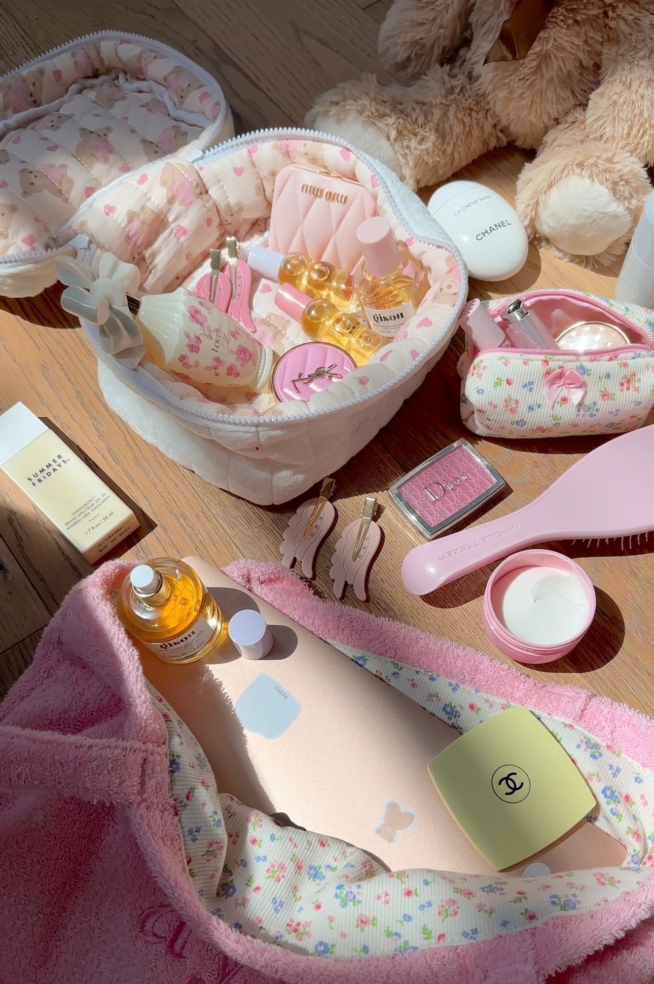 Open white plush vanity bag with pink heart print lining and multiple small beauty bottles inside.