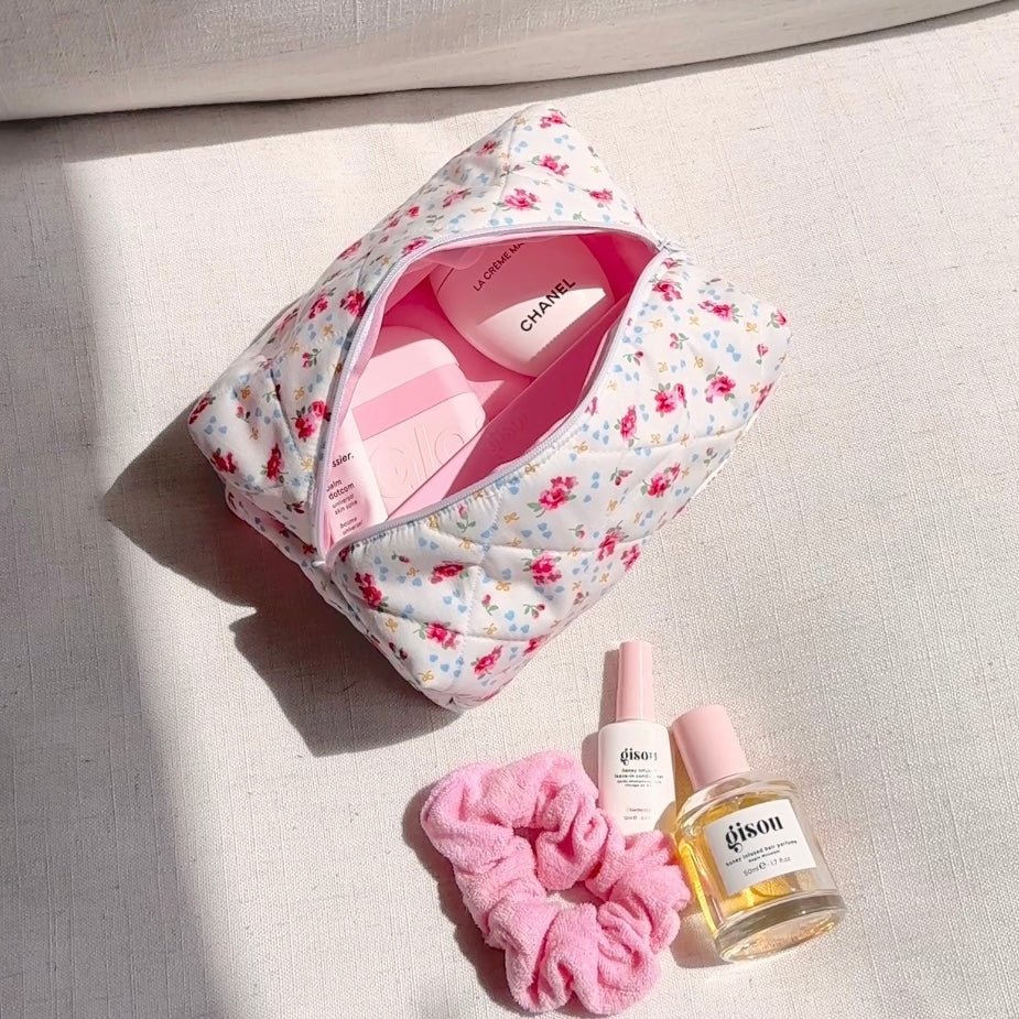 White floral zip pouch with front zipper open, interior showing pink bottles and products