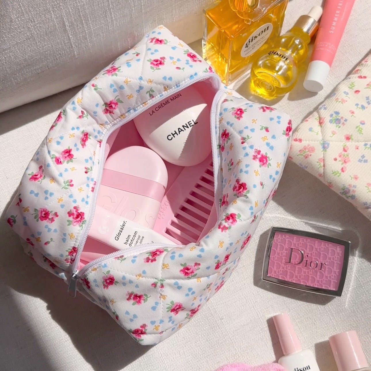White floral zip pouch open at top, showing interior lining with pink comb and bottles