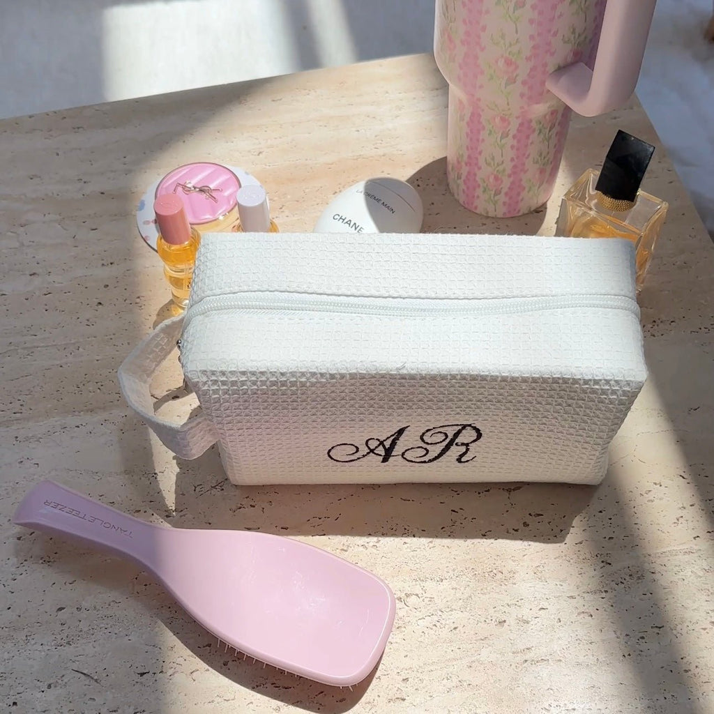 White waffle knit zip pouch with black monogram and curved top handle loop.