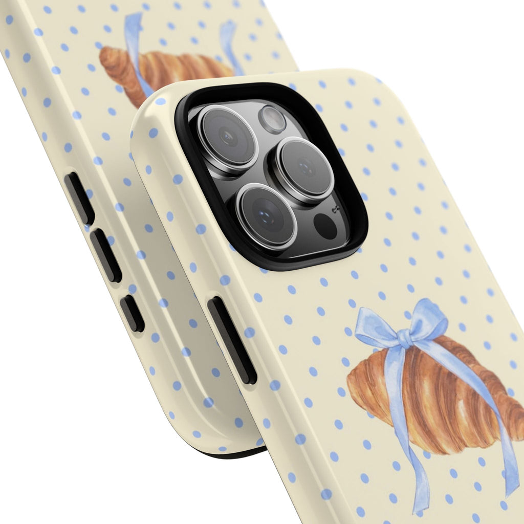 Angled view: cream case with blue polka dots, croissant bow detail, camera cutout