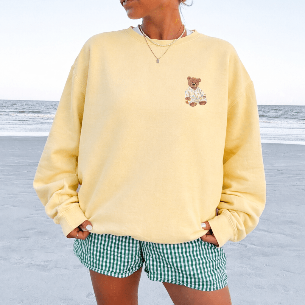 Yellow crewneck sweatshirt on model, teddy bear chest graphic, long sleeves
