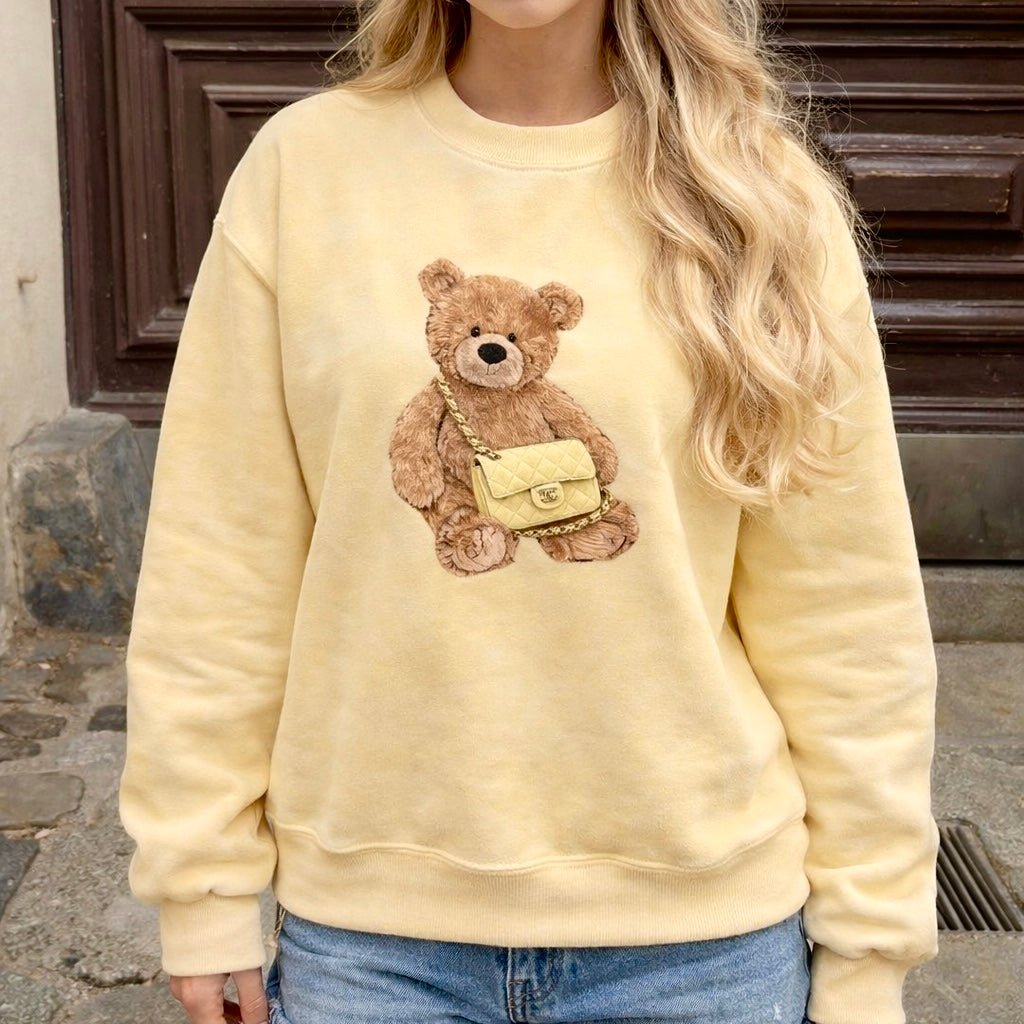 Model wearing yellow teddy bear crewneck sweatshirt, brown teddy appliqué center