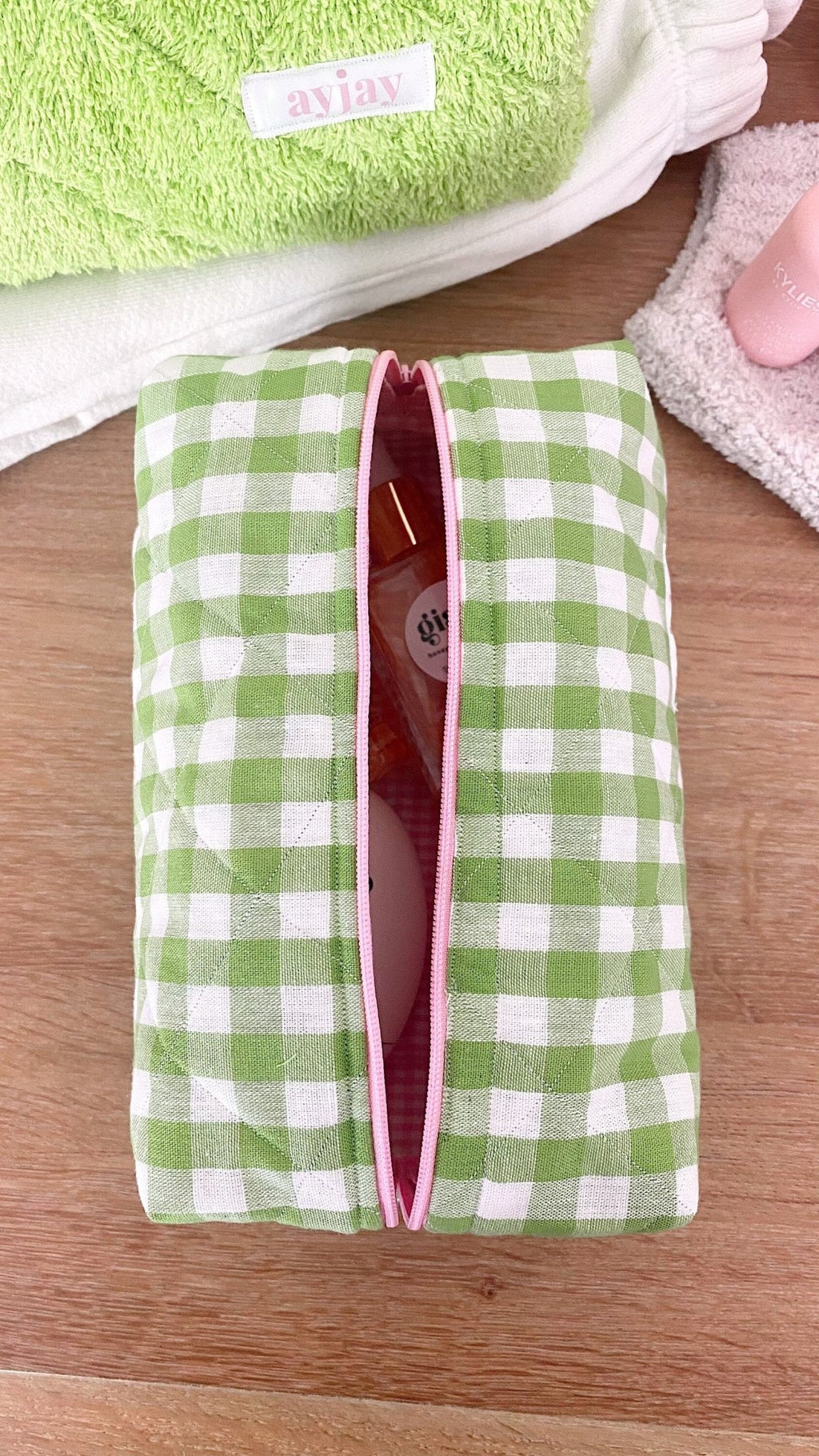 Green gingham zip pouch with pink-trim edge on folded towels
