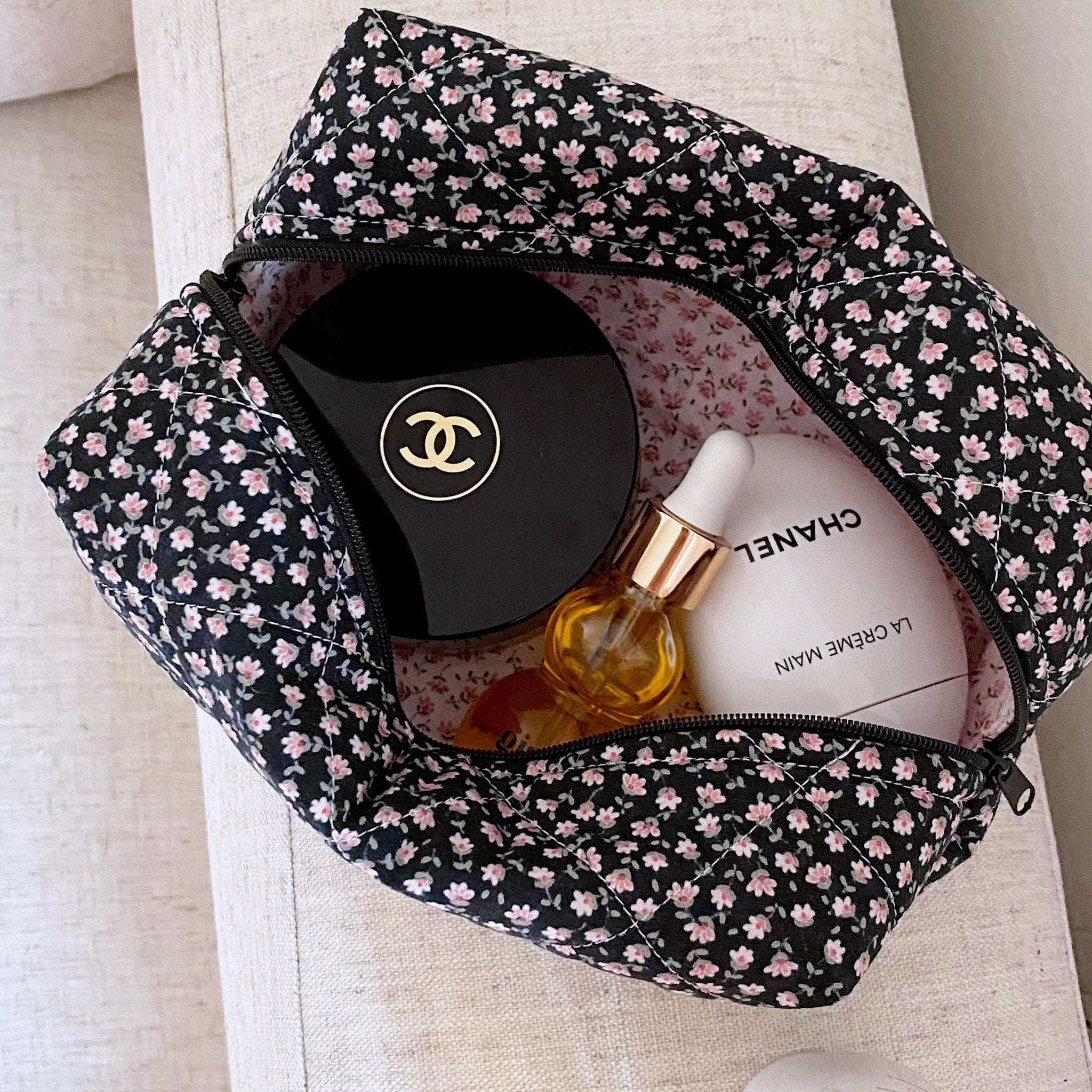Black ditsy floral cosmetic pouch with top zipper, open to show compartments and bottles