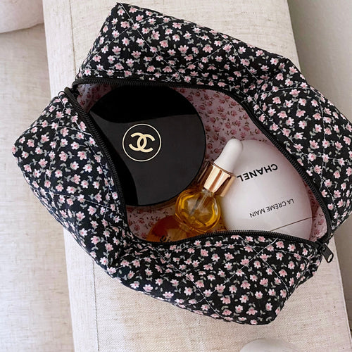 Black ditsy floral cosmetic pouch with top zipper, open to show compartments and bottles