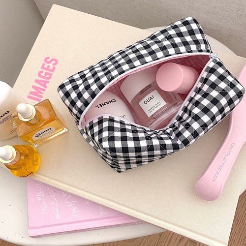 Black-and-white gingham zip pouch with top opening, holding beauty bottles inside