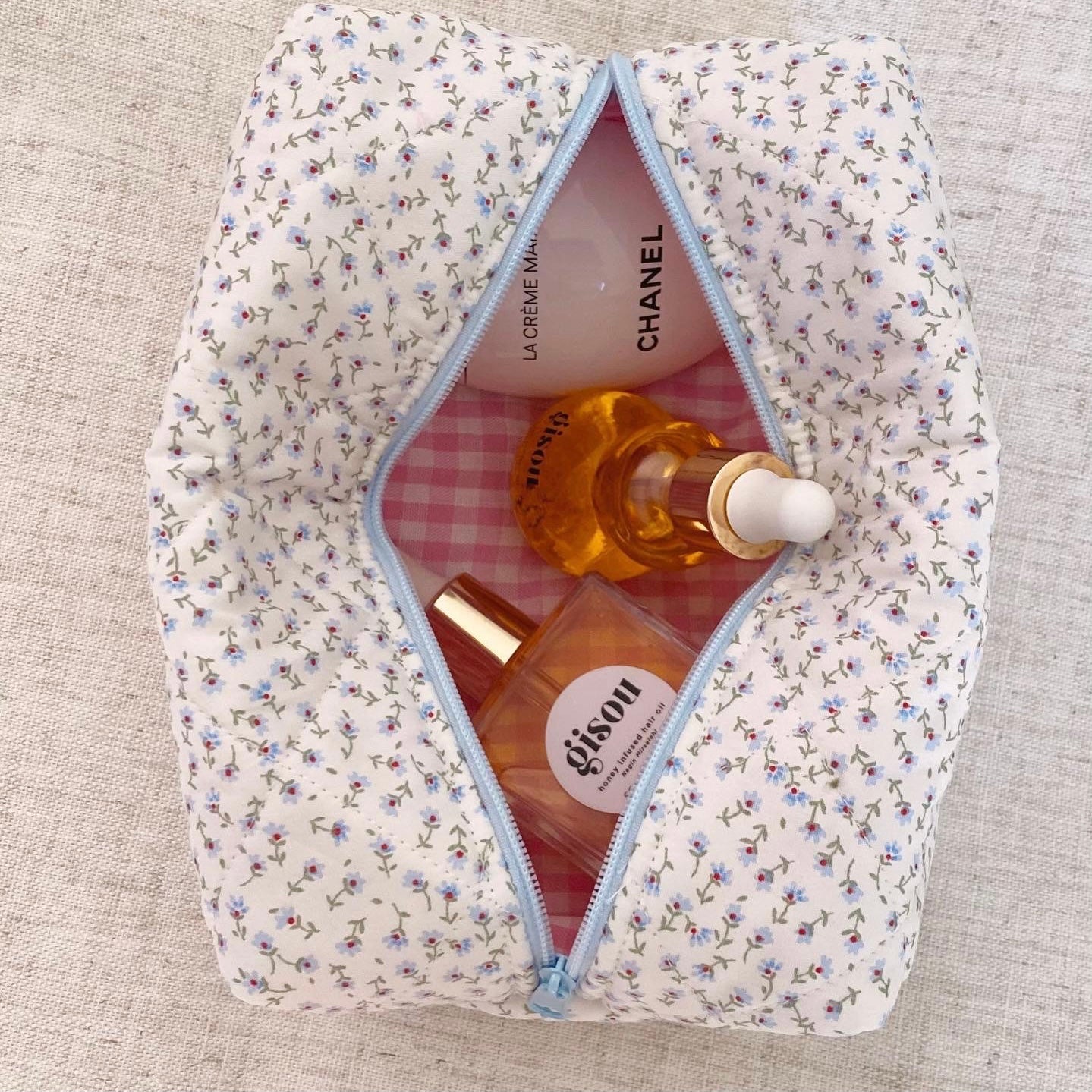 Blue ditsy floral zip pouch open, light-blue zipper and pink check lining with perfume bottles
