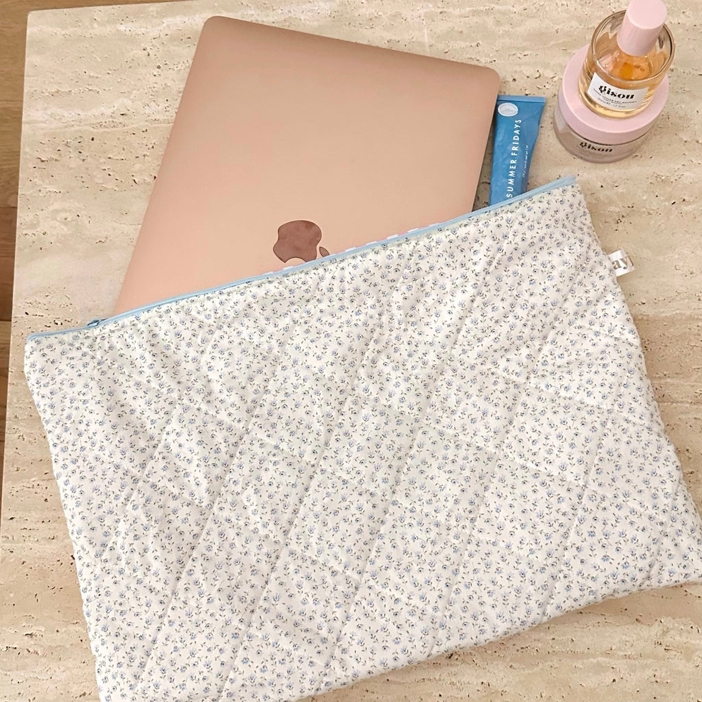 Blue ditsy floral zip pouch with blue piping along the opening; flat lay.