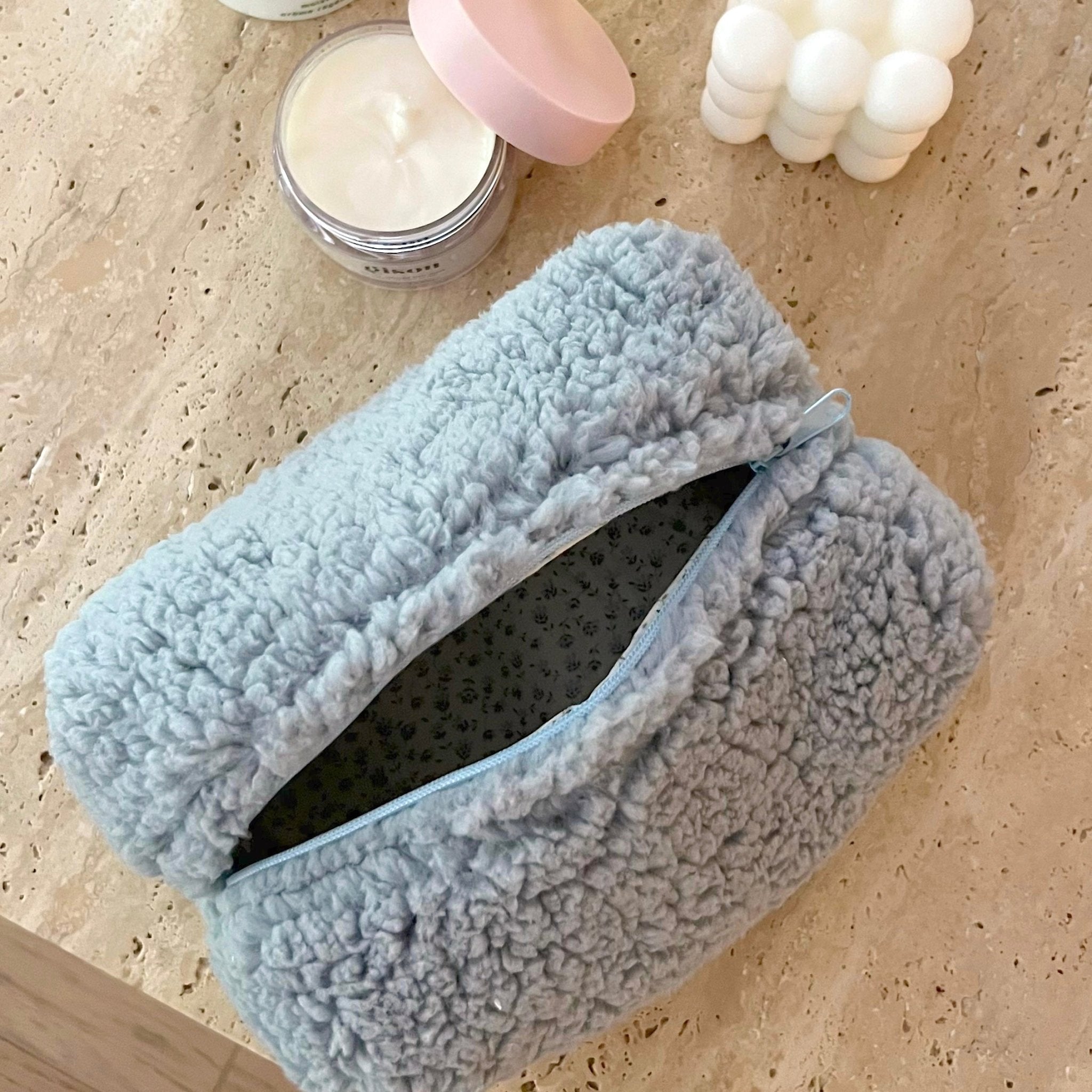 Light blue plush teddy pouch with blue trim, open showing floral lining inside