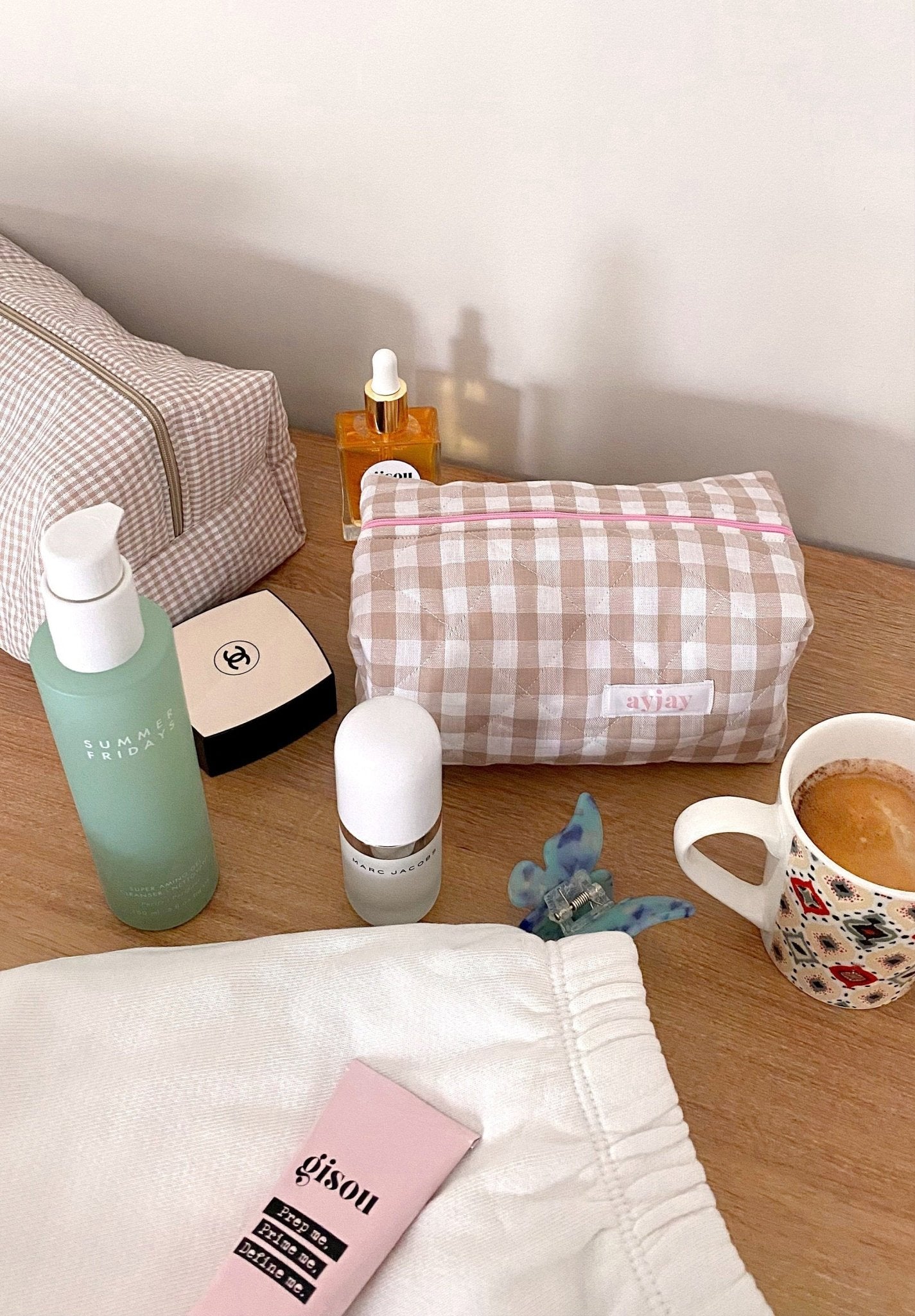 Brown gingham zip pouch with pink trim beside folded cloth and skincare bottles