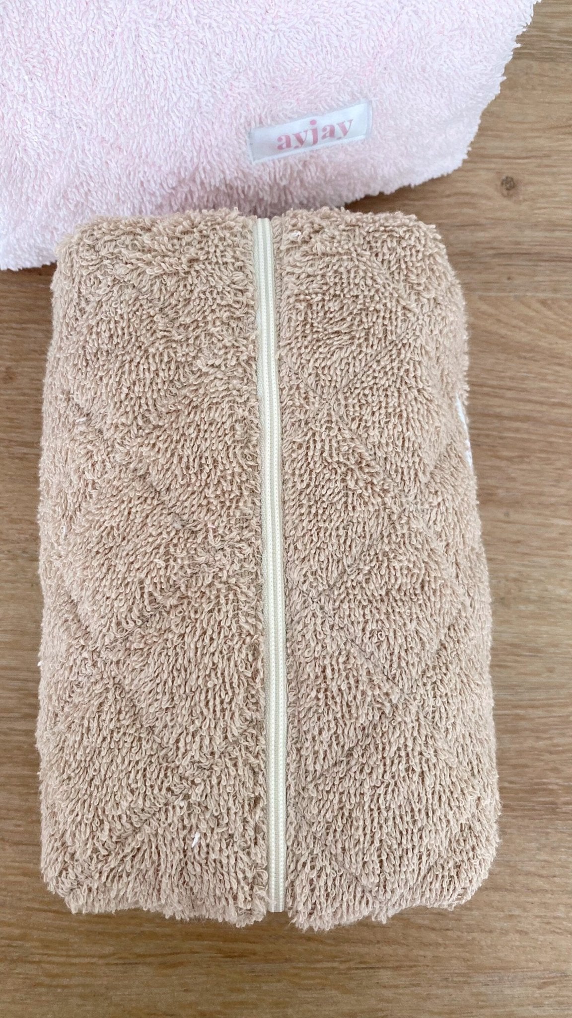 Beige terrycloth zip pouch, full-length zipper and label patch on top edge
