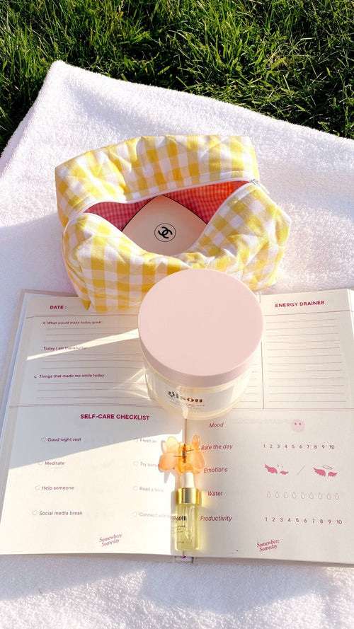 Butter yellow gingham pouch open on grass, with self-care checklist and small bottle