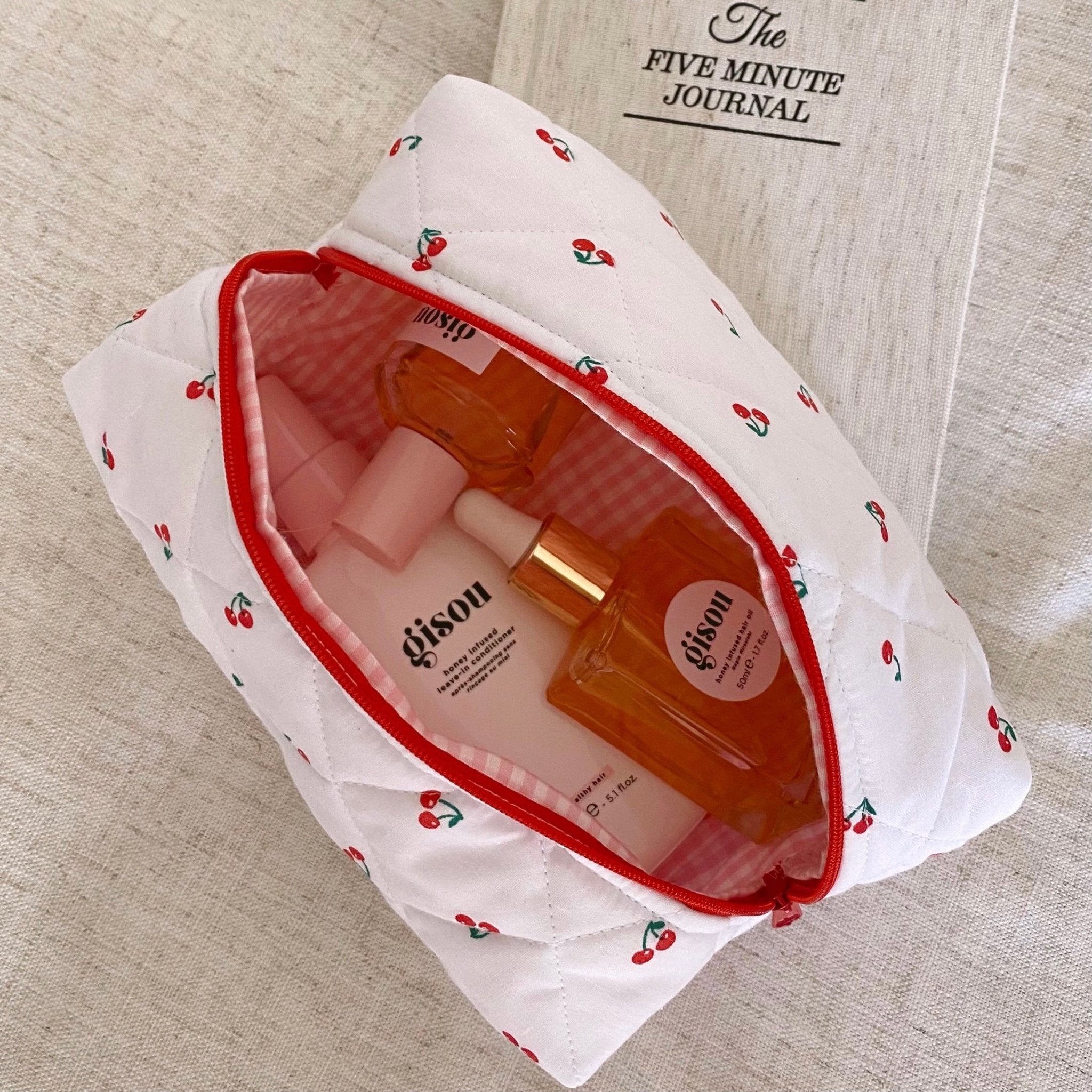White cherry print zip pouch with red lining, open top, showing bottles inside