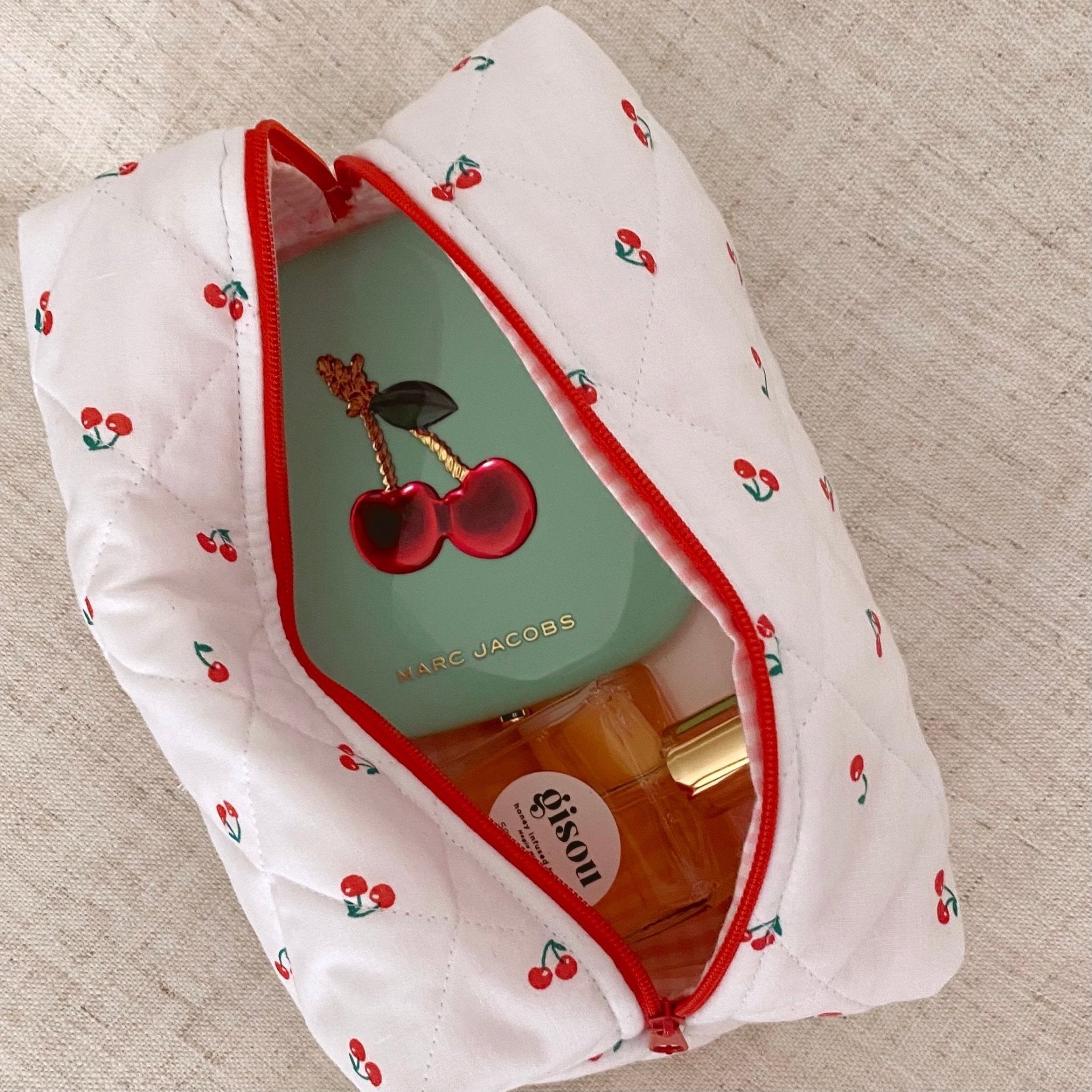 Open cherry print pouch with red trim and heart-shaped keychain, showing bottles inside