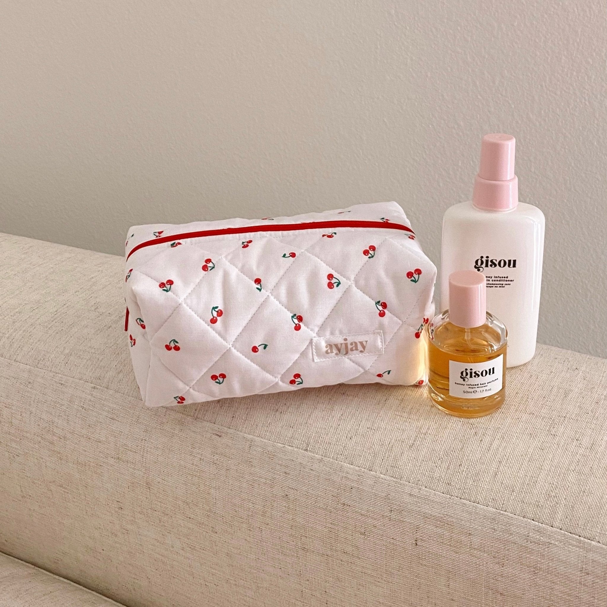 Quilted white cherry zip pouch with red trim on a bench with toiletries nearby
