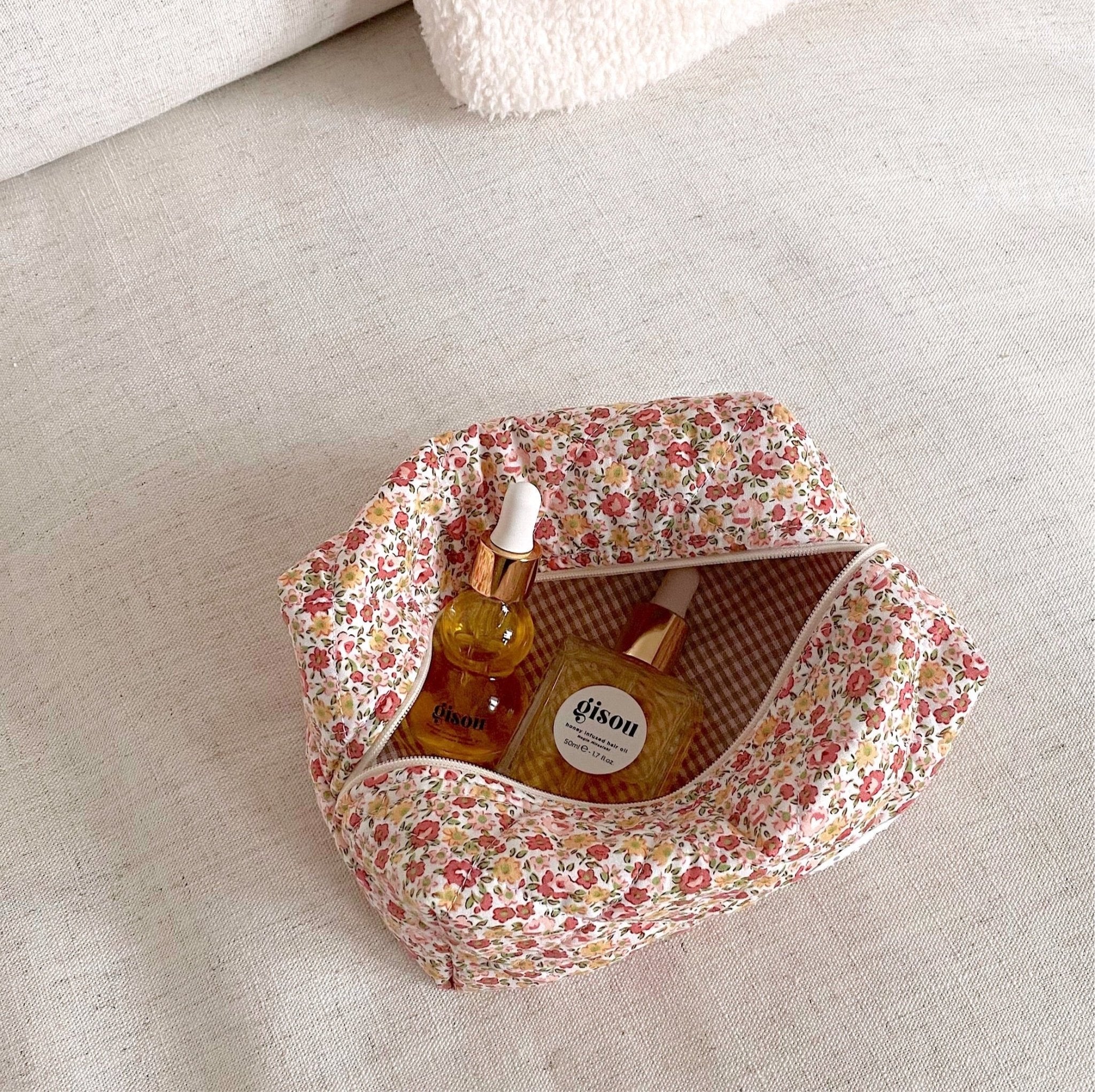 White floral zip pouch with red/brown flowers, open with bottles inside