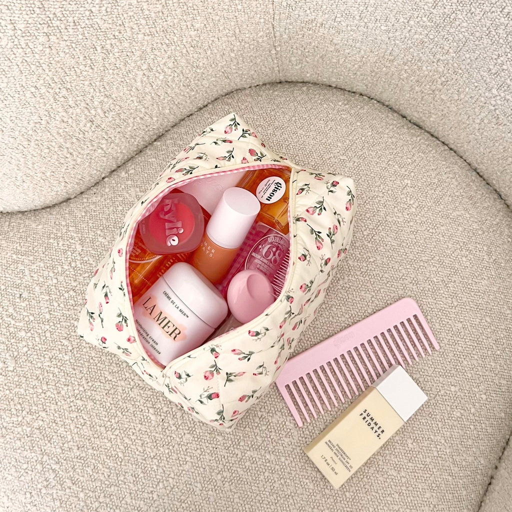 Cream floral zip pouch with pink trim, open top showing beauty products inside