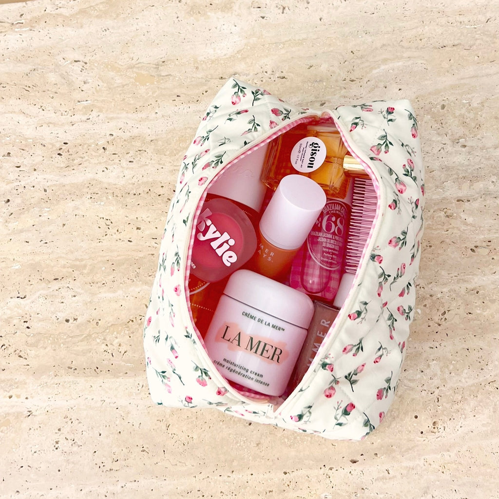 Cream floral zip pouch with pink trim, open top showing beauty products inside