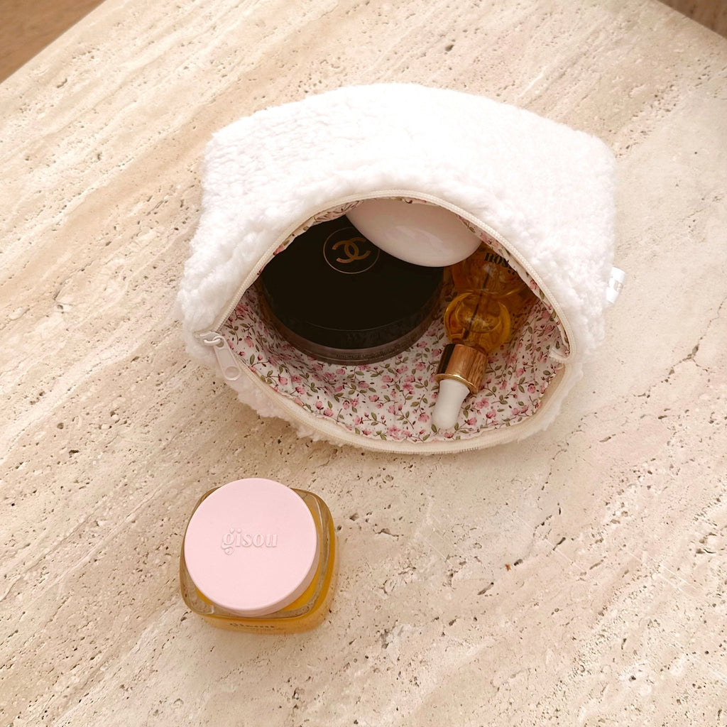 Cream teddy cosmetic pouch with pink floral lining, open mouth holding bottle and compact