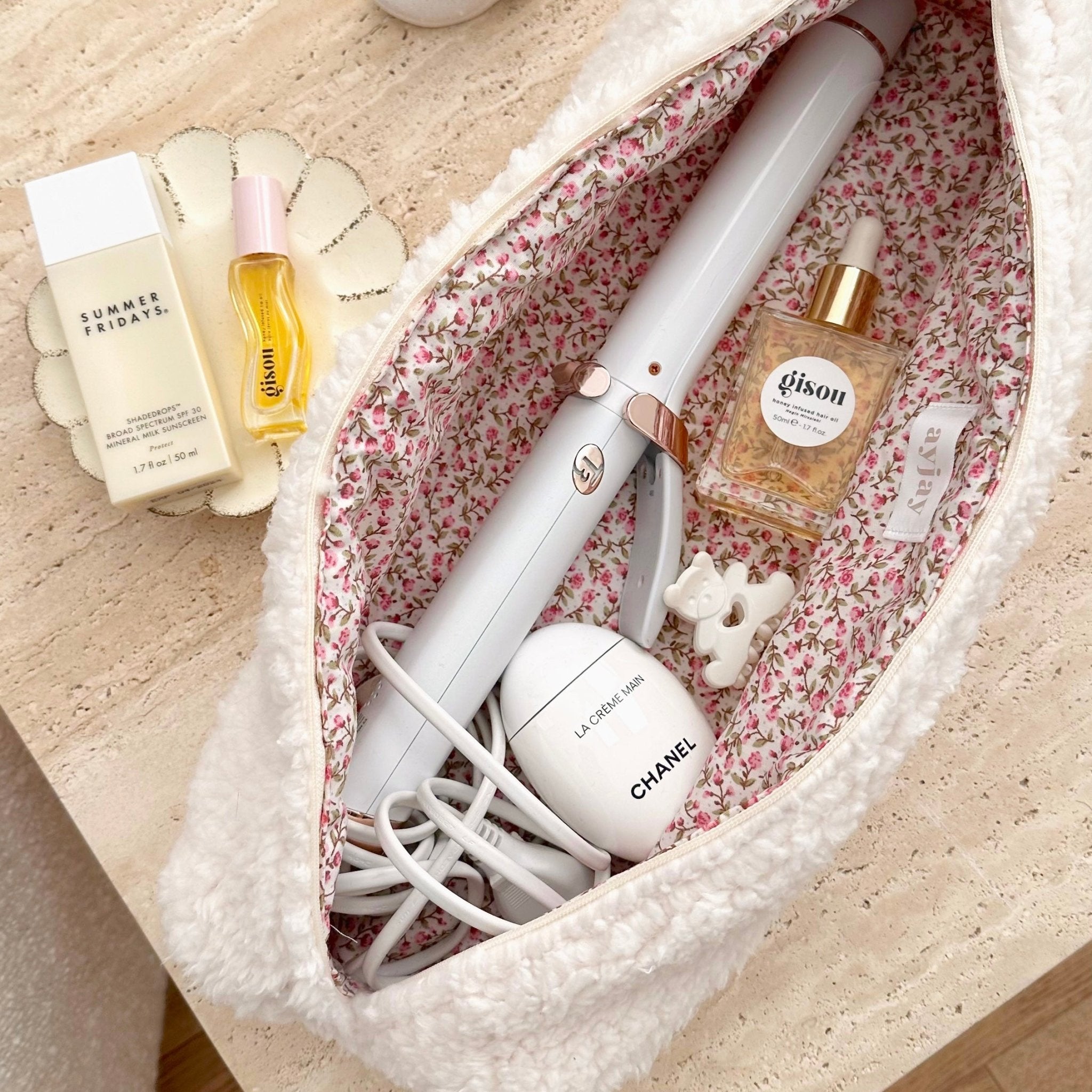 Cream soft teddy pouch with pink floral lining, open top showing interior items and cables