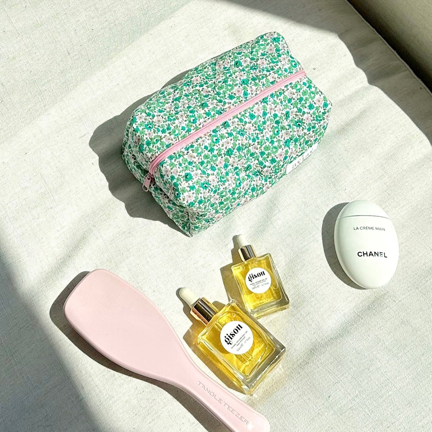 Green and pink floral zip pouch lying closed with pink zipper trim, on white fabric