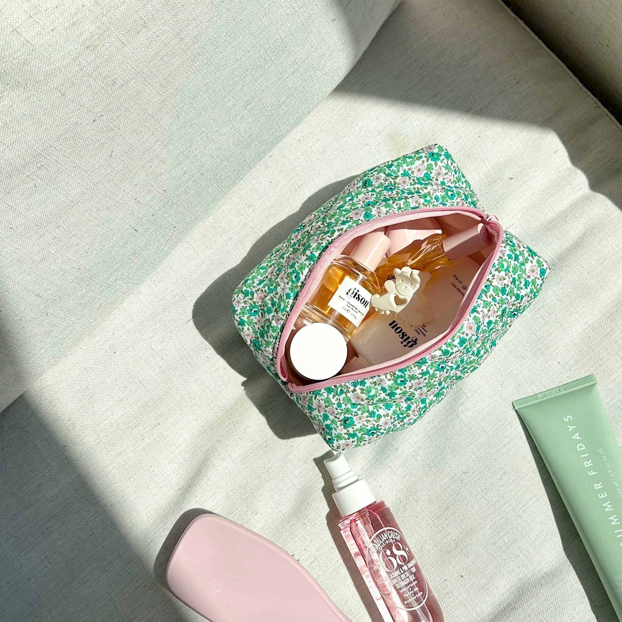 Green and pink floral cosmetic pouch open, pink trim, showing assorted beauty bottles
