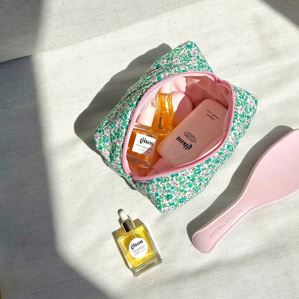 Green and pink floral cosmetic pouch open with pink lining, showing skincare bottles inside